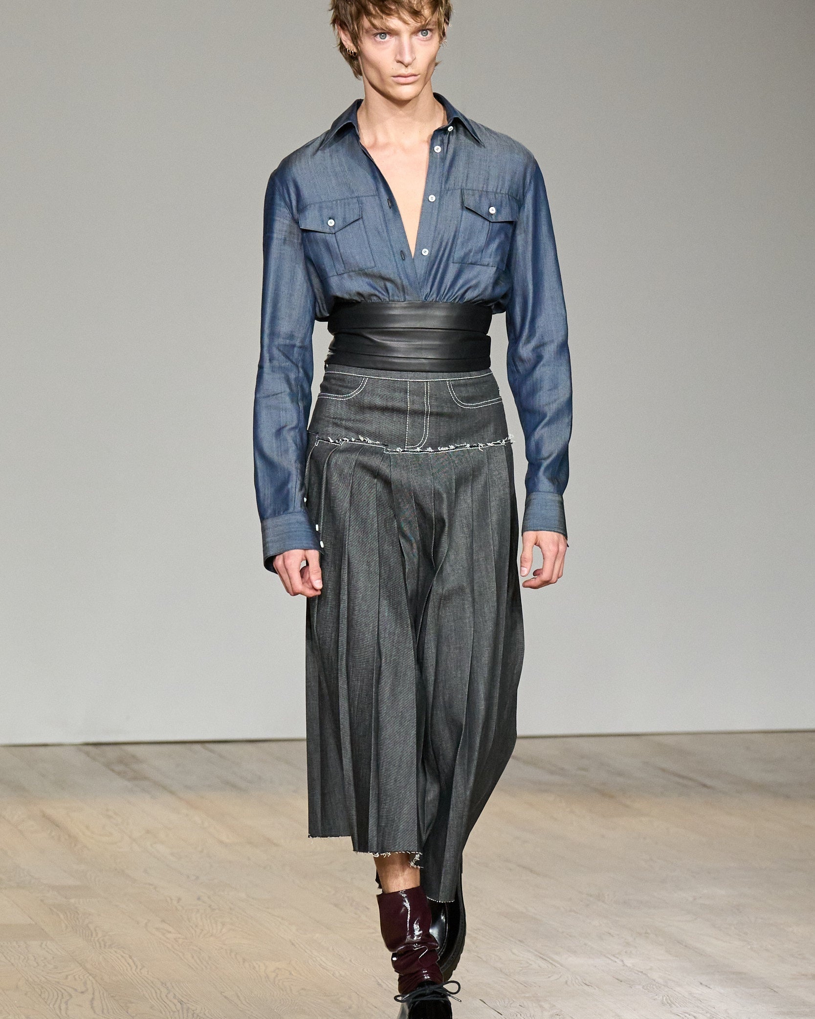 Model walking runway wearing Midnight Blue Shirt with Leather Waistband styled with high-waisted charcoal pleated pants and glossy black shoes, highlighting SHAO New York bespoke tailoring and luxury designer fashion.