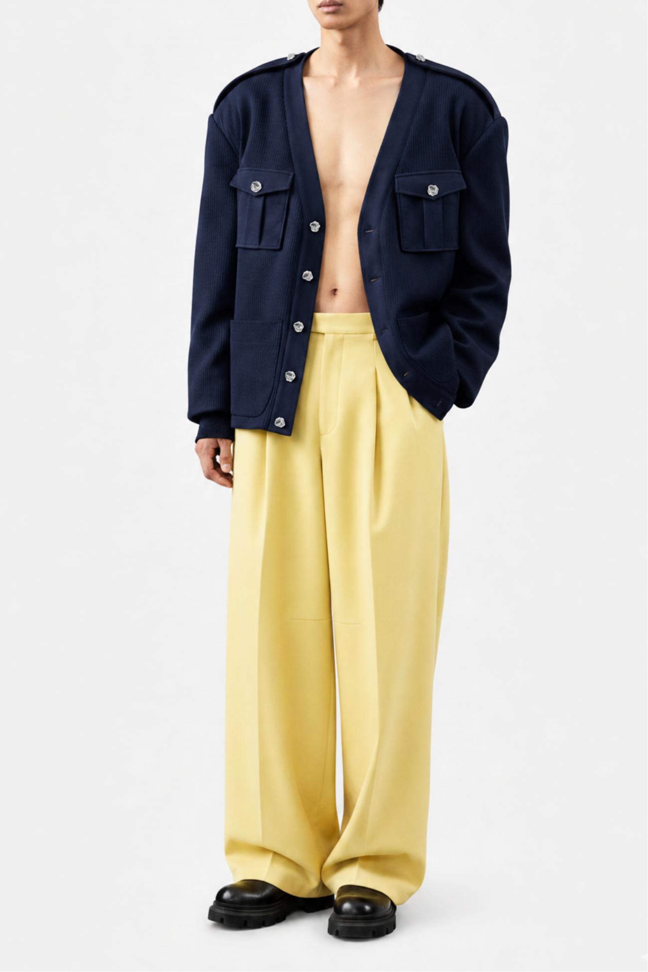 Model showcasing a Navy Military-Style Utility Cardigan with structured flap pockets and metal buttons, paired with wide-leg yellow trousers and black shoes, highlighting SHAO New York’s luxury designer fashion and sculptural silhouette.