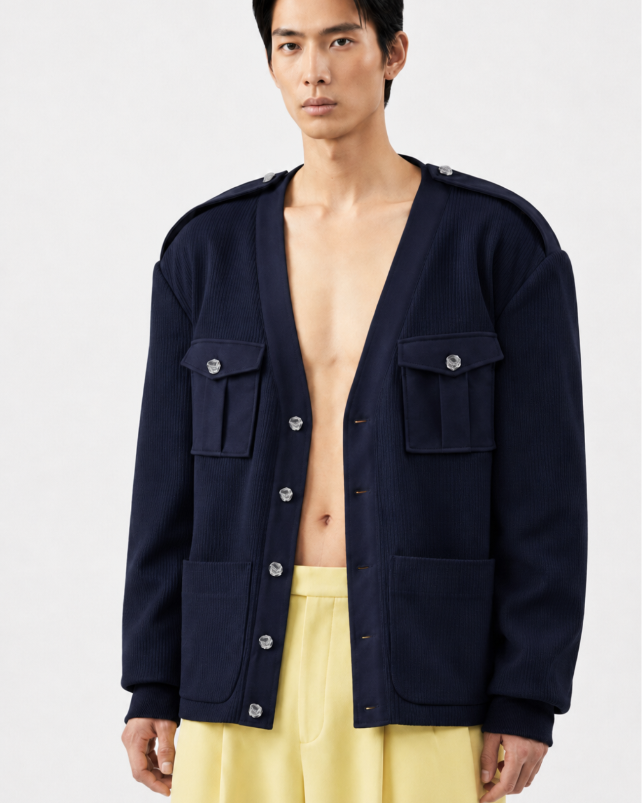 Model wearing a Navy Military-Style Utility Cardigan with structured flap pockets, decorative buttons, and shoulder epaulettes, styled open over bare skin for a modern sculptural silhouette.
