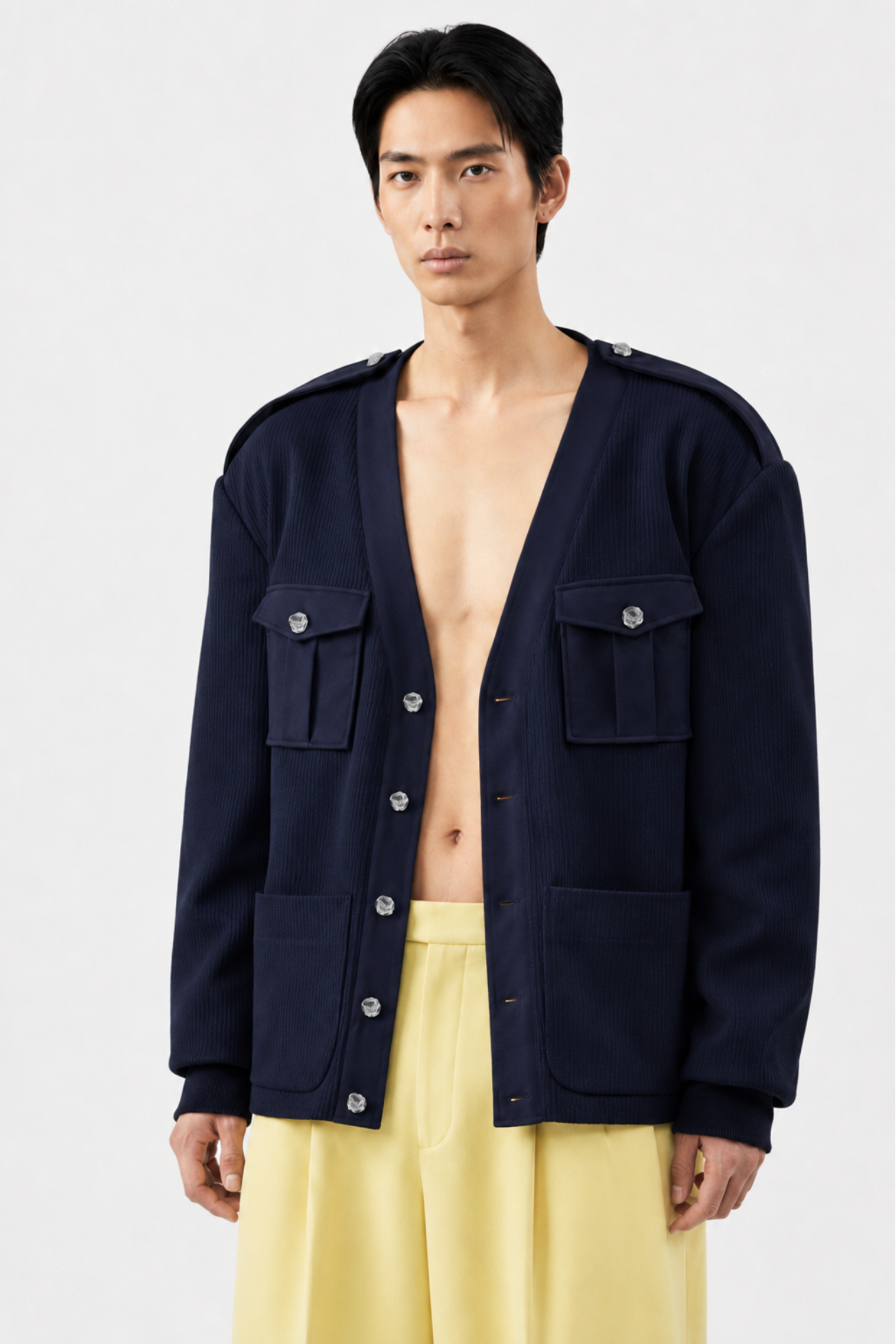 Model wearing a Navy Military-Style Utility Cardigan with structured flap pockets, decorative buttons, and shoulder epaulettes, styled open over bare skin for a modern sculptural silhouette.