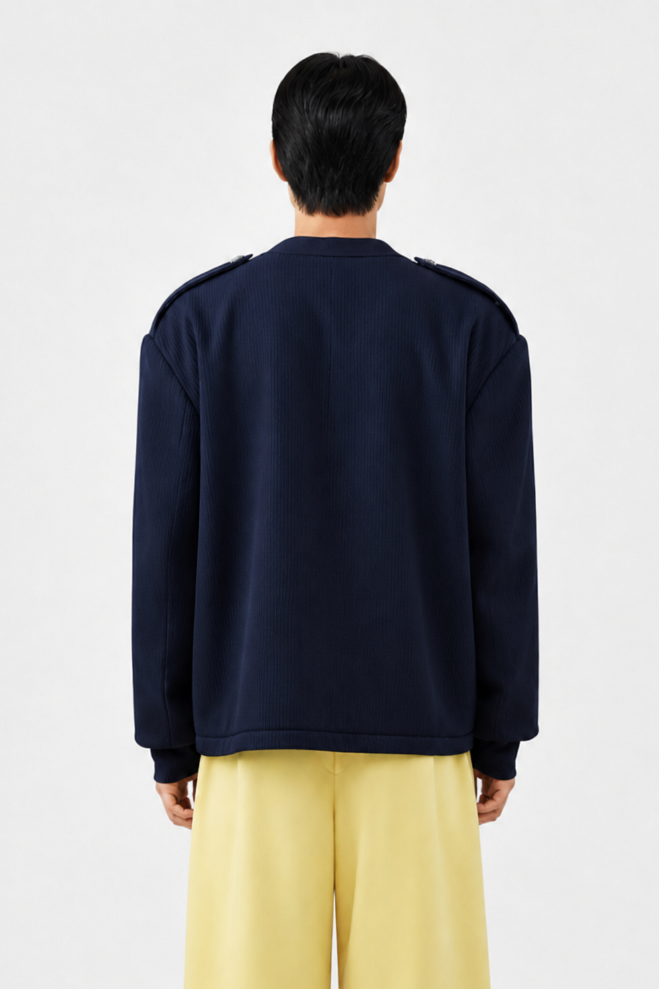 Back view of a model wearing a Navy Military-Style Utility Cardigan with structured shoulder epaulettes and a relaxed fit, paired with wide-leg yellow trousers for a refined sculptural silhouette.