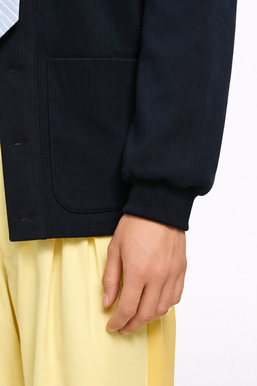 Close-up of a model’s hand beside the detailed front patch pocket and ribbed cuff of a dark navy jacket, paired with bright Ion Yellow Two-Tone Wide-Leg Trousers, illustrating SHAO New York’s luxury designer fashion and sculptural silhouette.