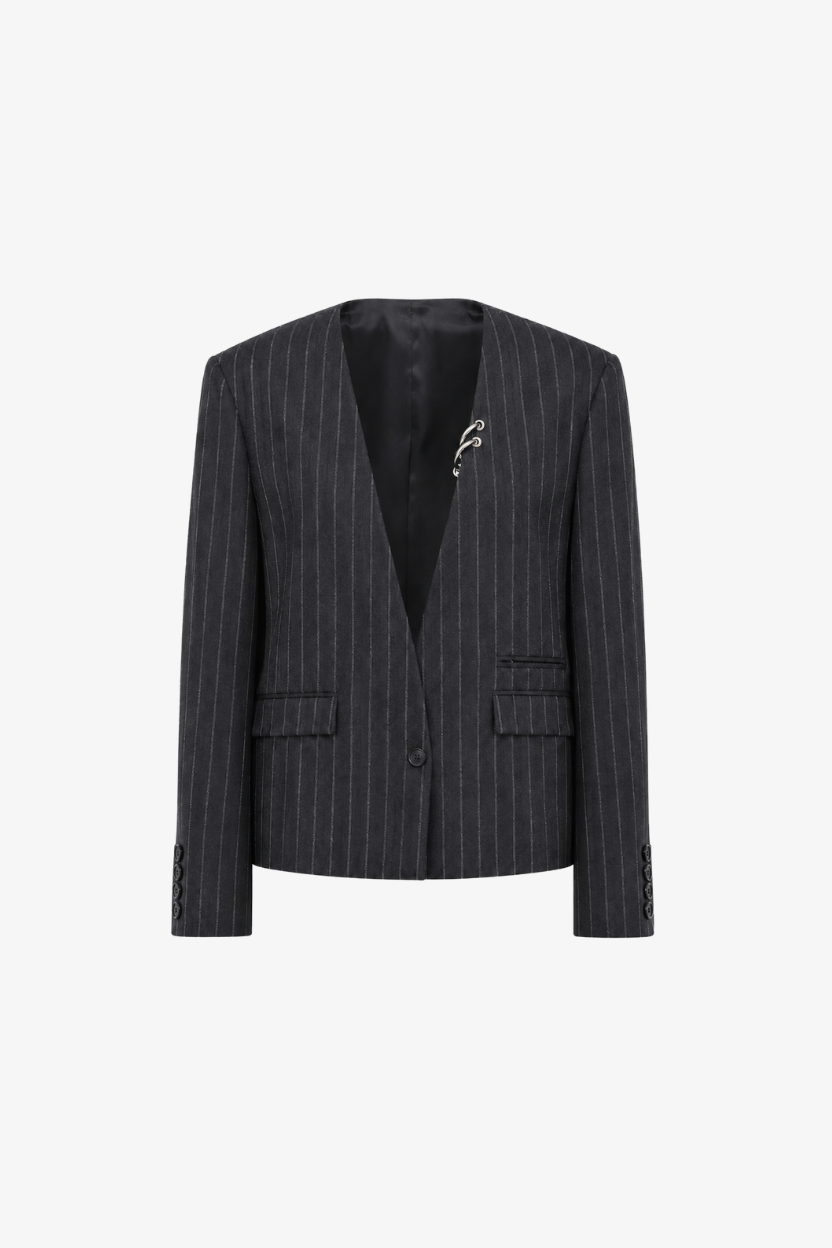 A dark gray pinstripe blazer with a black interior lining and a small silver graphic brooch on the left chest, displayed against a solid white background.