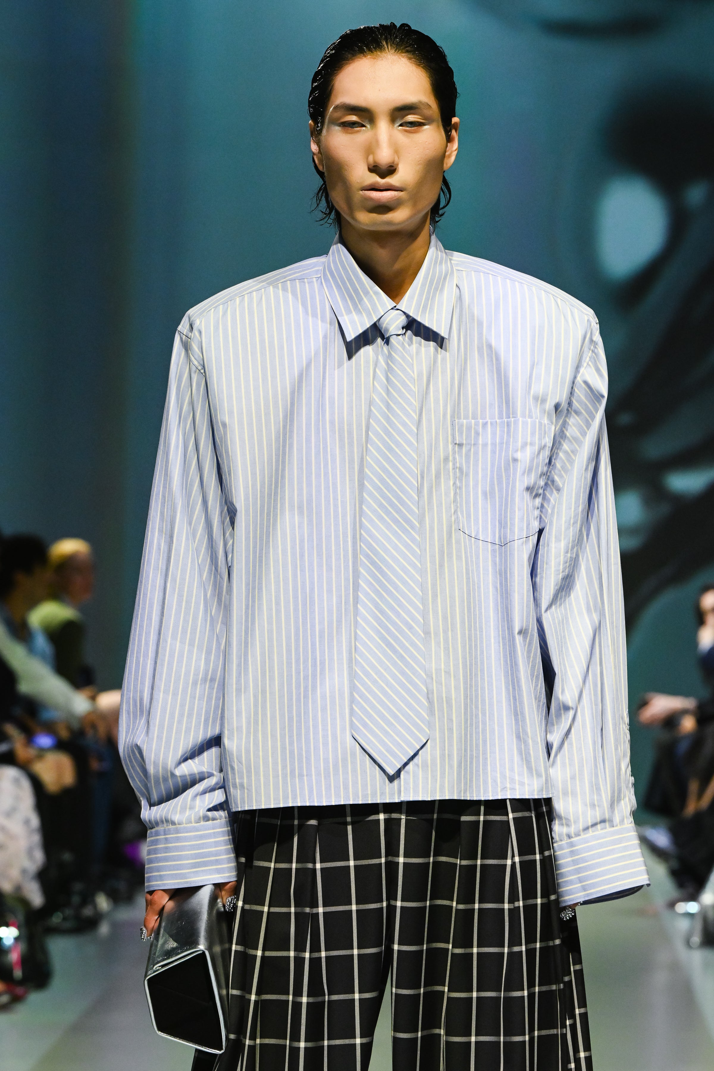 Model wearing Windowpane Wide-Leg Double-Pleated Trousers with a black and white grid pattern paired with an oversized blue and white striped shirt and matching tie, showcasing bespoke tailoring and a sculptural silhouette in luxury designer fashion.