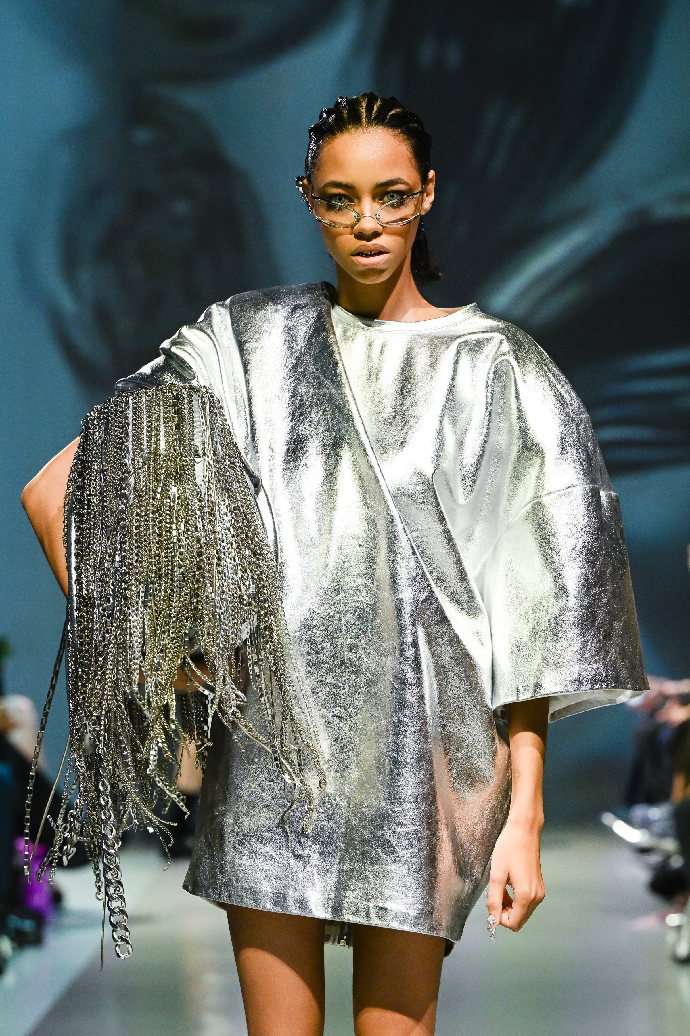 Model wearing the Silver Metallic Leather Mini Dress with a loose sculptural silhouette, featuring shiny reflective leather and an oversized fringe chain accessory, showcasing SHAO New York bespoke tailoring.