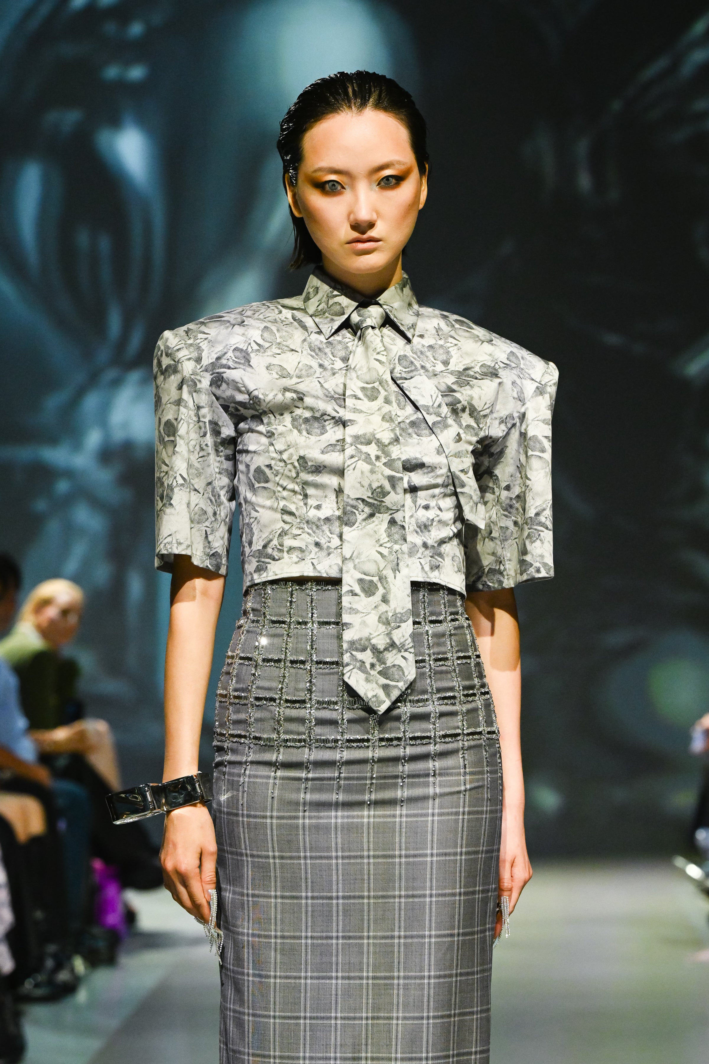 Model wearing a patterned top and plaid skirt on a runway
