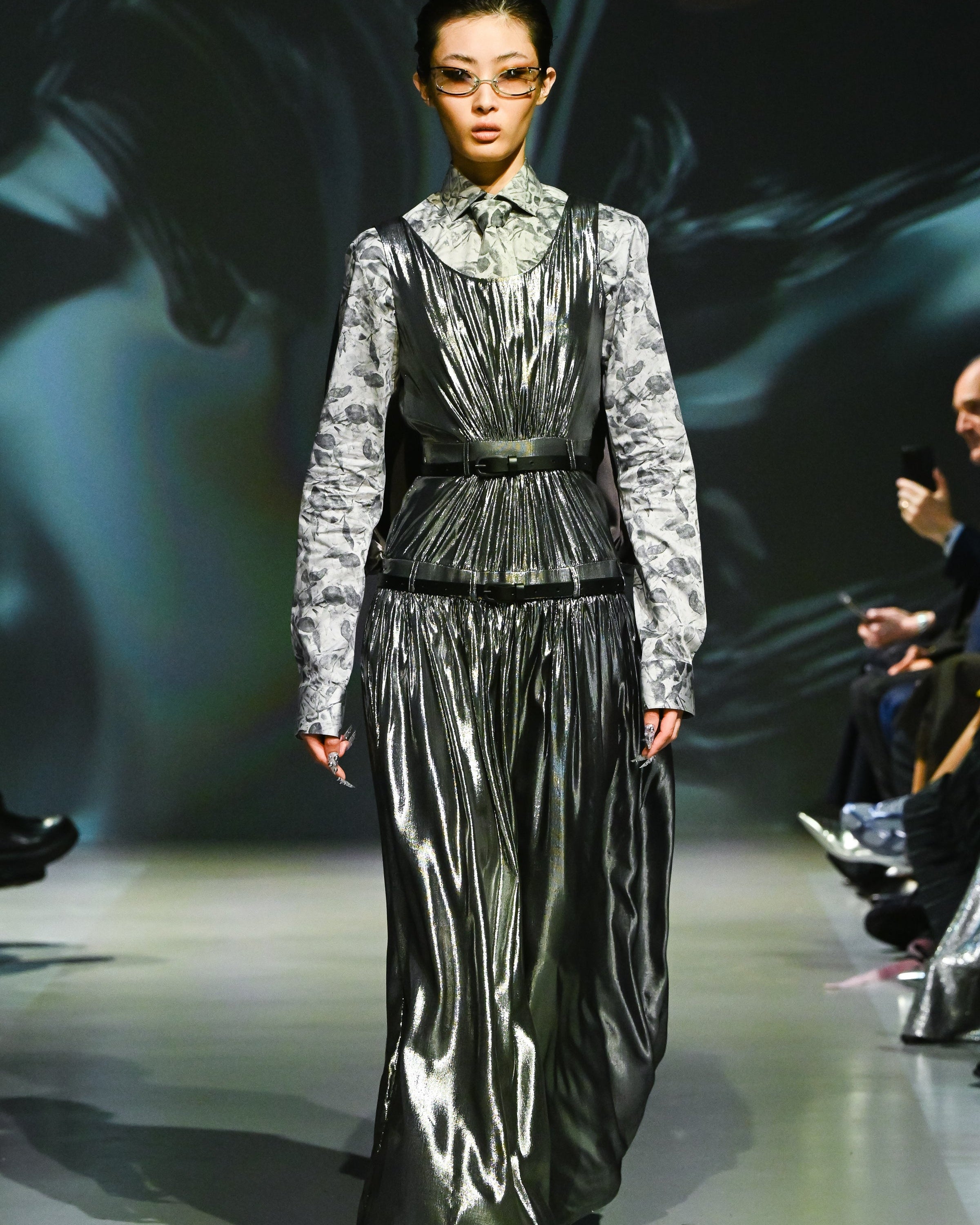 Model wearing a layered metallic dress with a gathered skirt and a floral long-sleeve shirt underneath, cinched at the waist by a Matte Black Leather Belt, embodying modern luxury designer fashion.