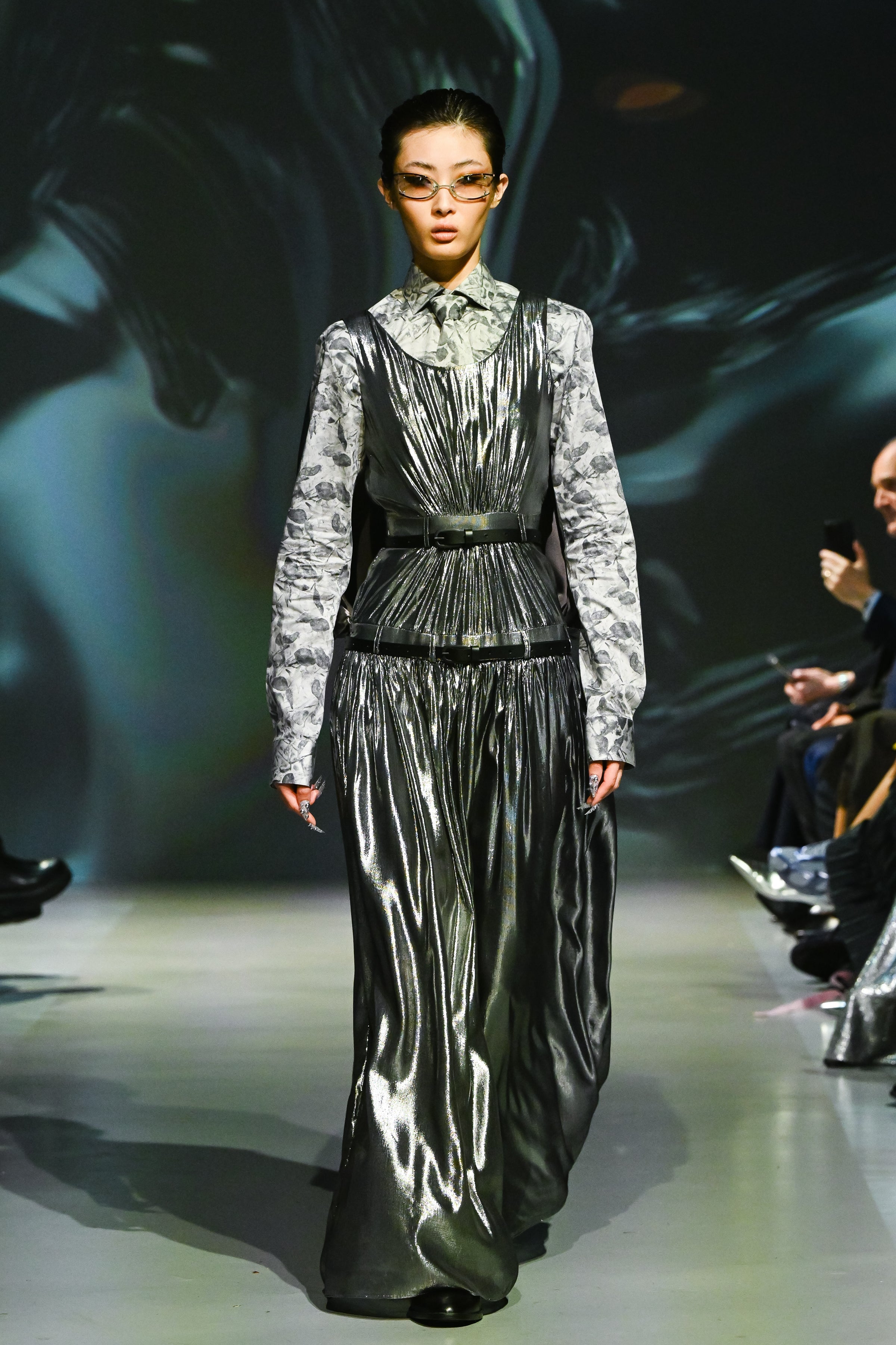 Model wearing a layered metallic dress with a gathered skirt and a floral long-sleeve shirt underneath, cinched at the waist by a Matte Black Leather Belt, embodying modern luxury designer fashion.