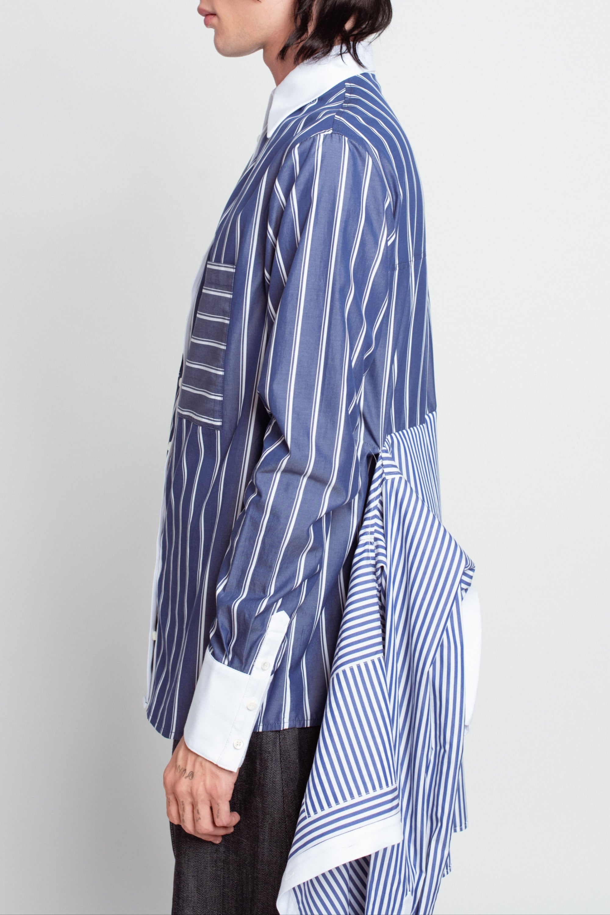 Side profile of model wearing Blue Pinstripe Layered Shirt – Attached Back Construction, featuring vertical pinstripes and an extended back panel for a sculptural, bespoke tailored silhouette.