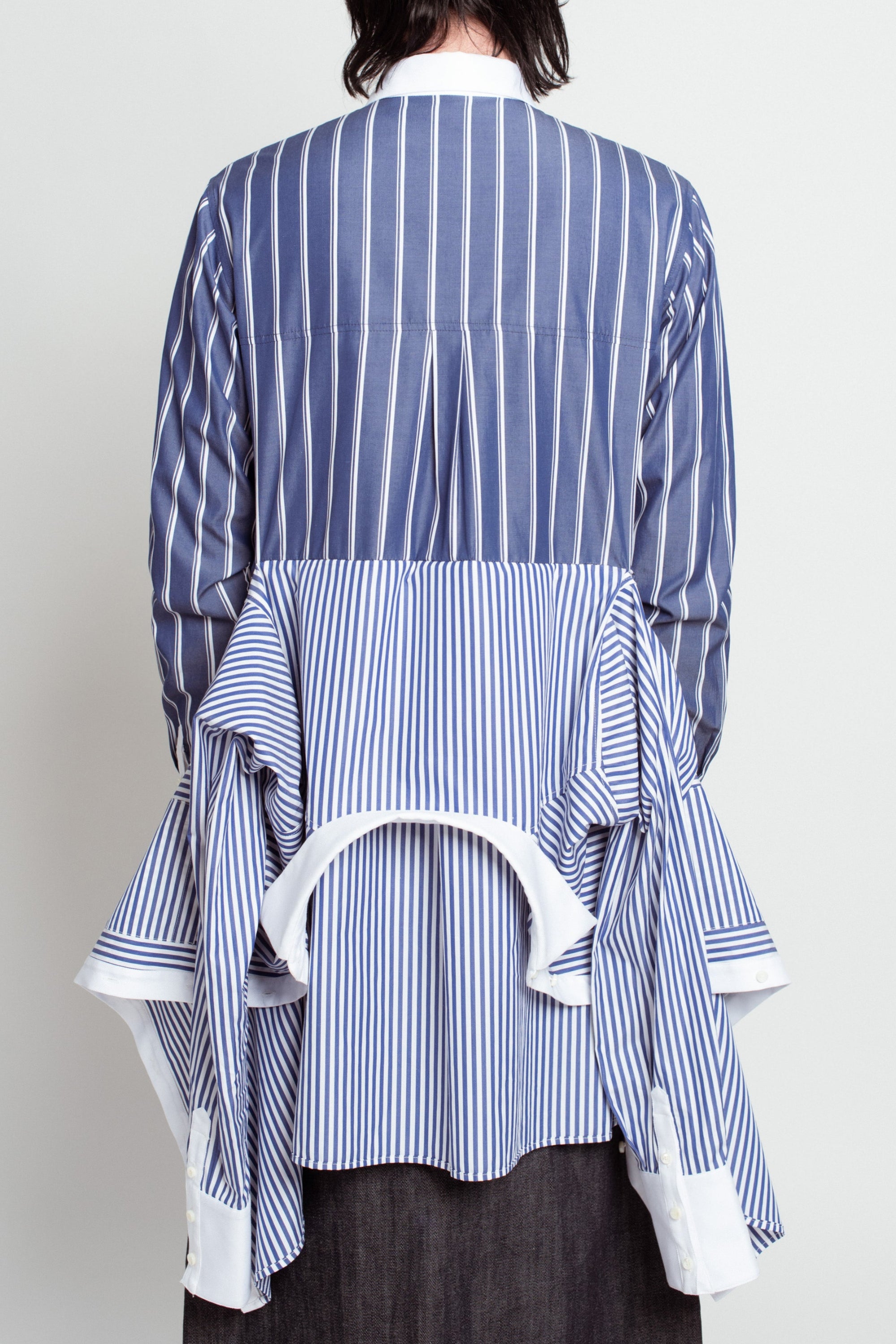 Back view of Blue Pinstripe Layered Shirt – Attached Back Construction featuring mixed vertical and horizontal stripes with an extended layered shirting detail creating a sculptural silhouette.