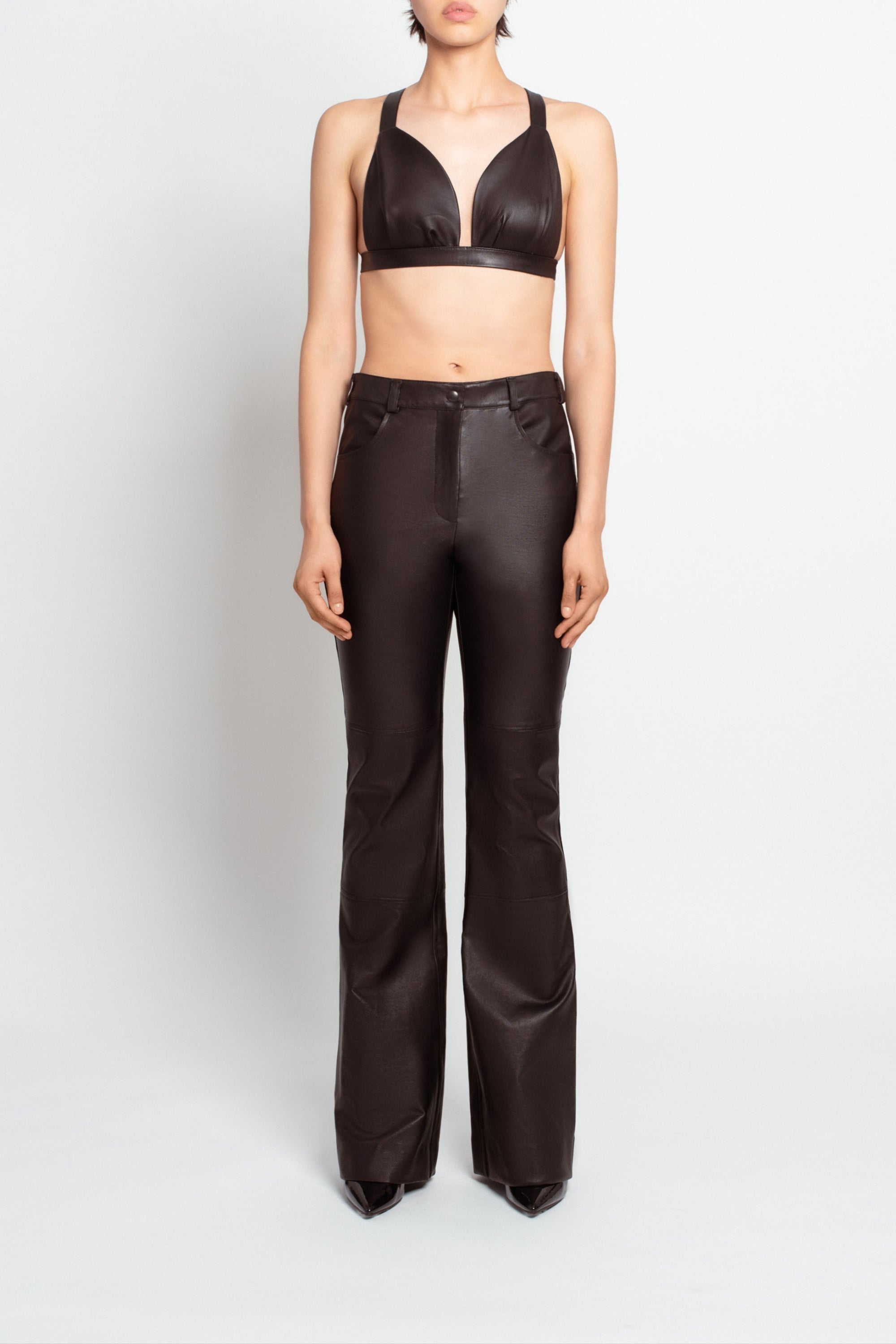 Front view of model wearing Jet Black Leather Bustier – Architectural Construction with a deep neckline and tailored fit, paired with high-waisted tapered pants for a sleek luxury designer fashion look.
