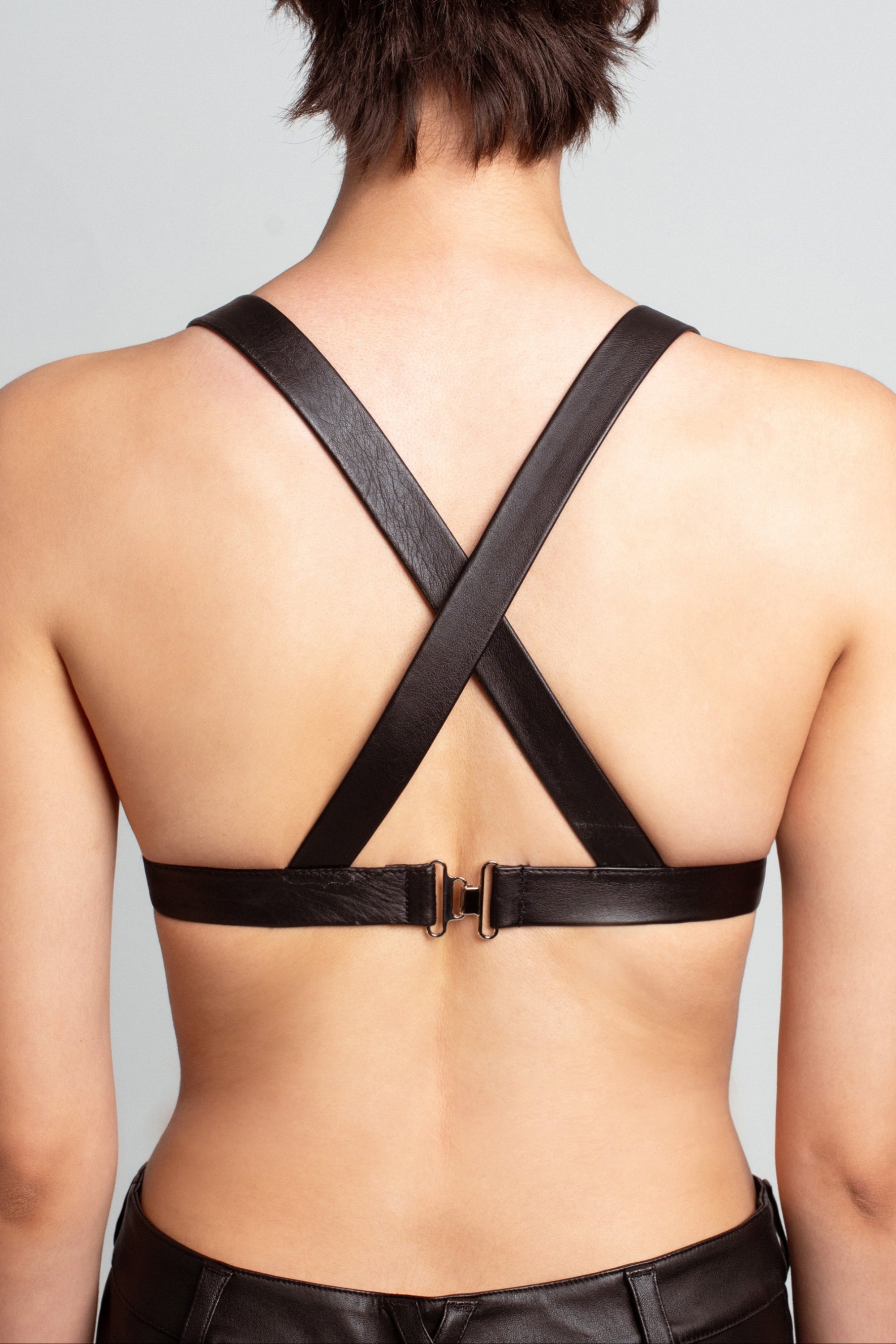 Back view of Jet Black Leather Bustier – Architectural Construction featuring wide crossed straps and a buckle closure, highlighting bespoke New York designer tailoring in a sleek sculptural silhouette.