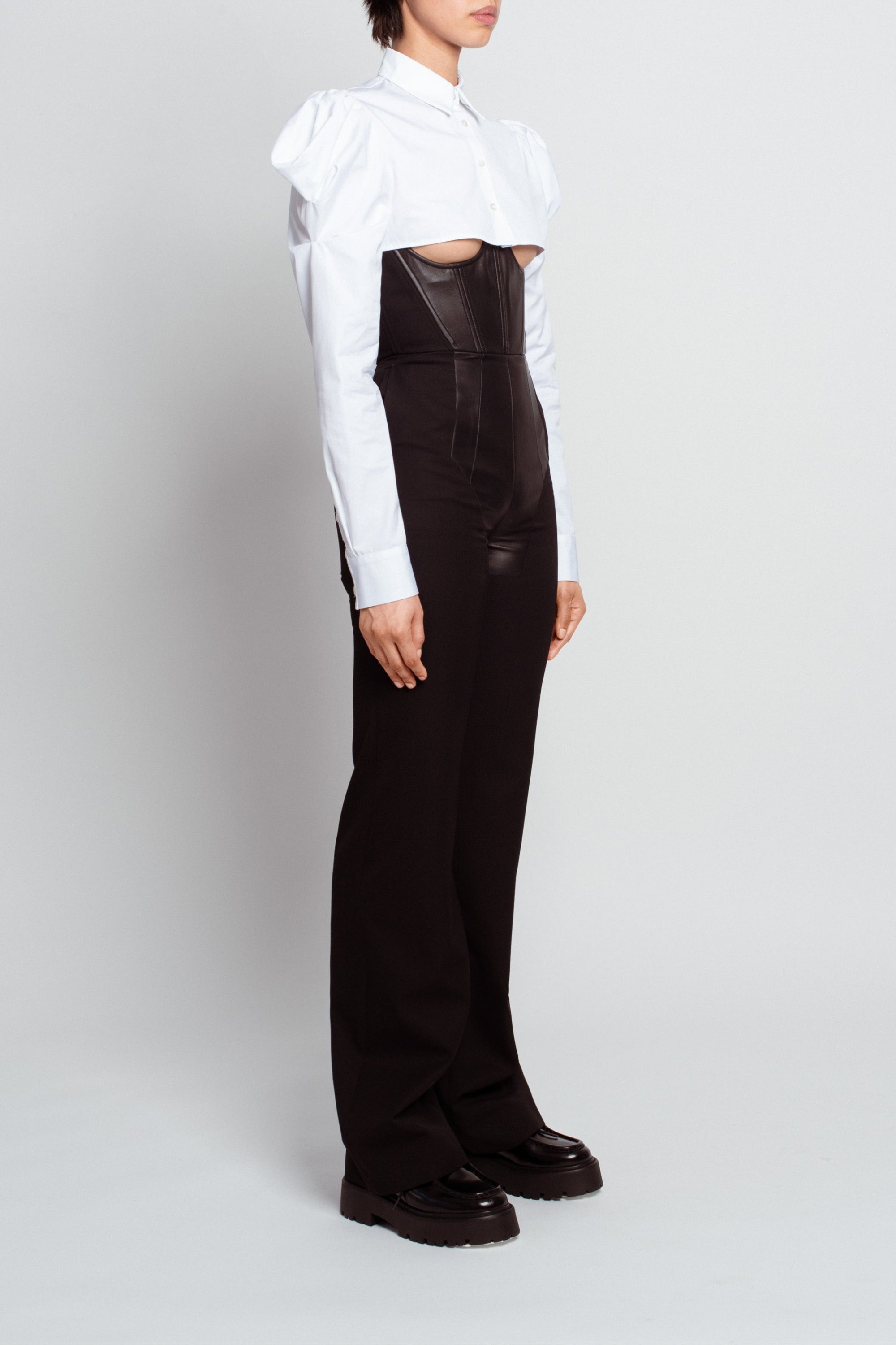 Side profile of Essential White Button-Up Shirt – Dramatic Puffed Shoulders featuring a cropped structured silhouette with pronounced puffed sleeves, paired with high-waist tailored black trousers, embodying luxury designer fashion and SHAO New York bespoke tailoring.