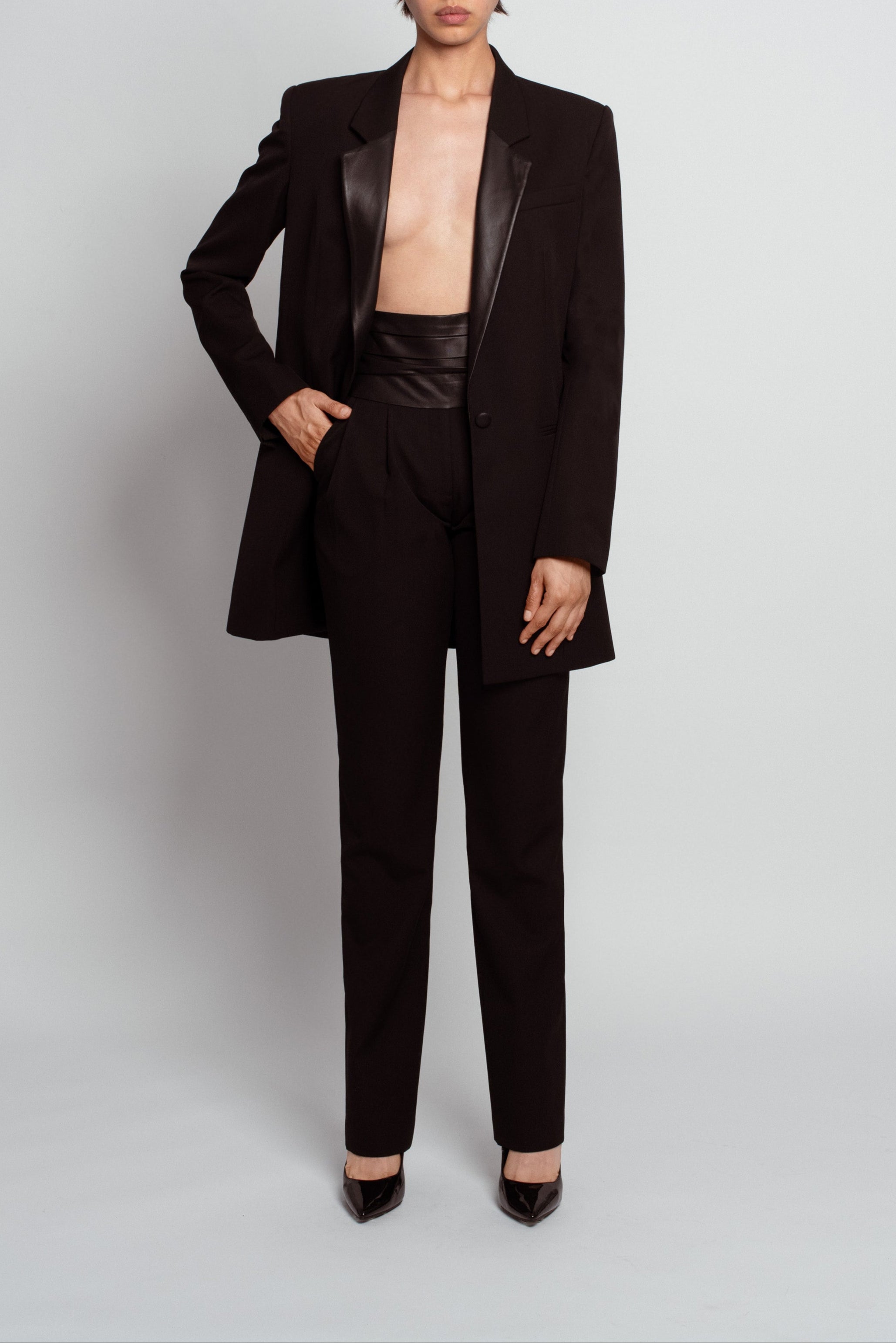 Front view of Jet Black Tailored Trousers – Leather Cummerbund Detail styled with a matching blazer featuring leather lapels, showcasing a sleek, sculptural silhouette in SHAO New York bespoke tailoring.