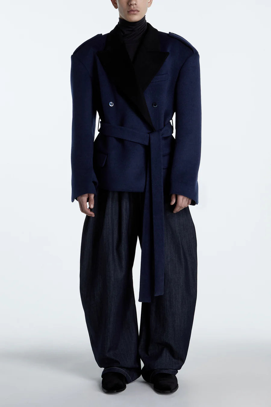 Front view of a model wearing an oversized navy blazer with structured shoulders, a wide belt, and black lapels paired with voluminous dark wide-leg trousers and black shoes.