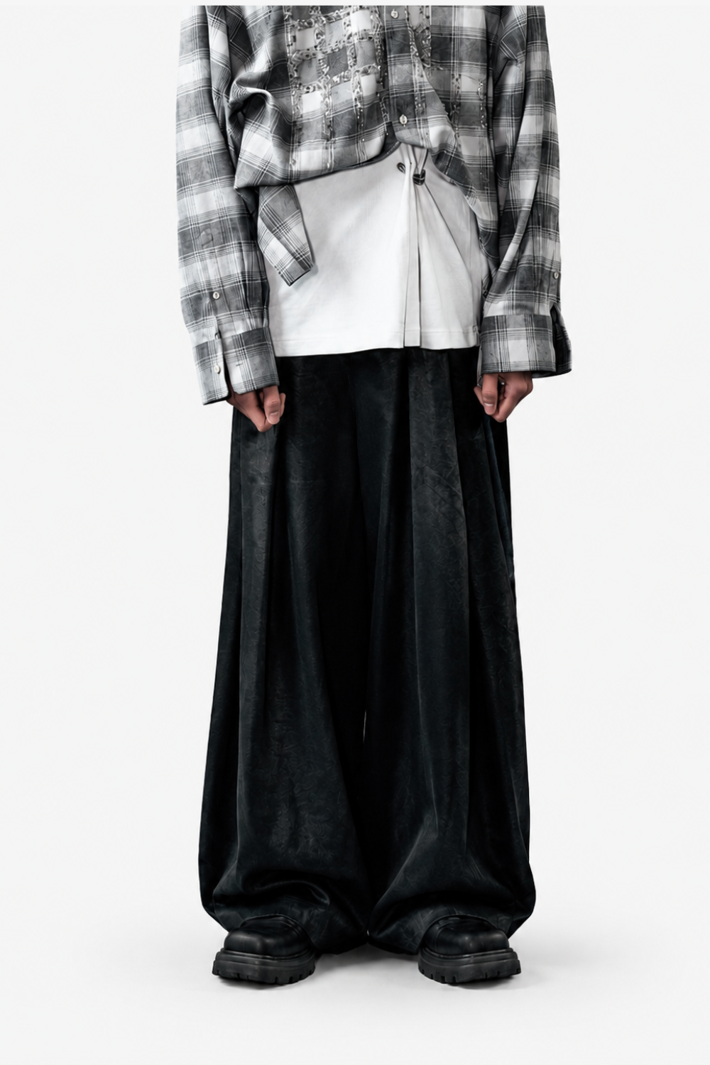 Model featuring the Pierced Vintage T-Shirt - White layered under a loose plaid shirt, paired with wide-legged black trousers and chunky black shoes, highlighting a contemporary sculptural silhouette.
