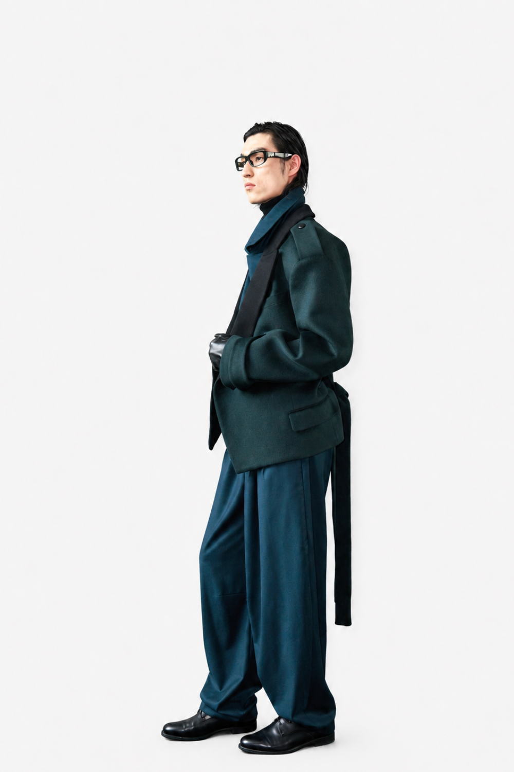 Model wearing Wool Barrel Pleated Trousers - Emerald styled with a tailored dark green jacket featuring a high collar and structured shoulders, paired with black leather gloves and sleek black footwear, embodying SHAO New York luxury designer fashion and a modern sculptural silhouette.