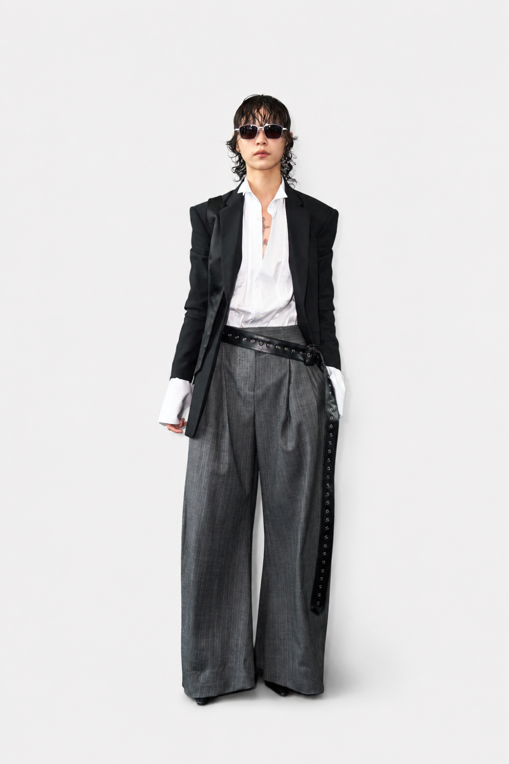 Model wearing Black Trompe L'Oeil Blazer with Satin Vest Overlay styled with a crisp white shirt featuring extended cuffs, paired with wide-leg gray tailored trousers and a long black leather belt, embodying SHAO New York luxury designer fashion and bespoke tailoring.