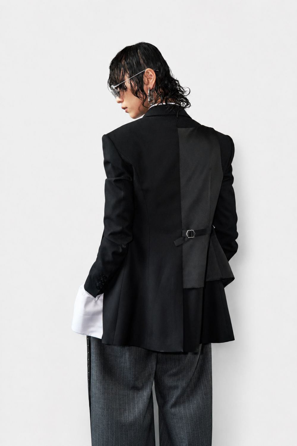 Model seen from behind wearing Black Trompe L'Oeil Blazer with Satin Vest Overlay, featuring tailored back buckle detail, paired with gray pinstripe trousers, showcasing SHAO New York bespoke tailoring and luxury designer fashion with a sculptural silhouette.