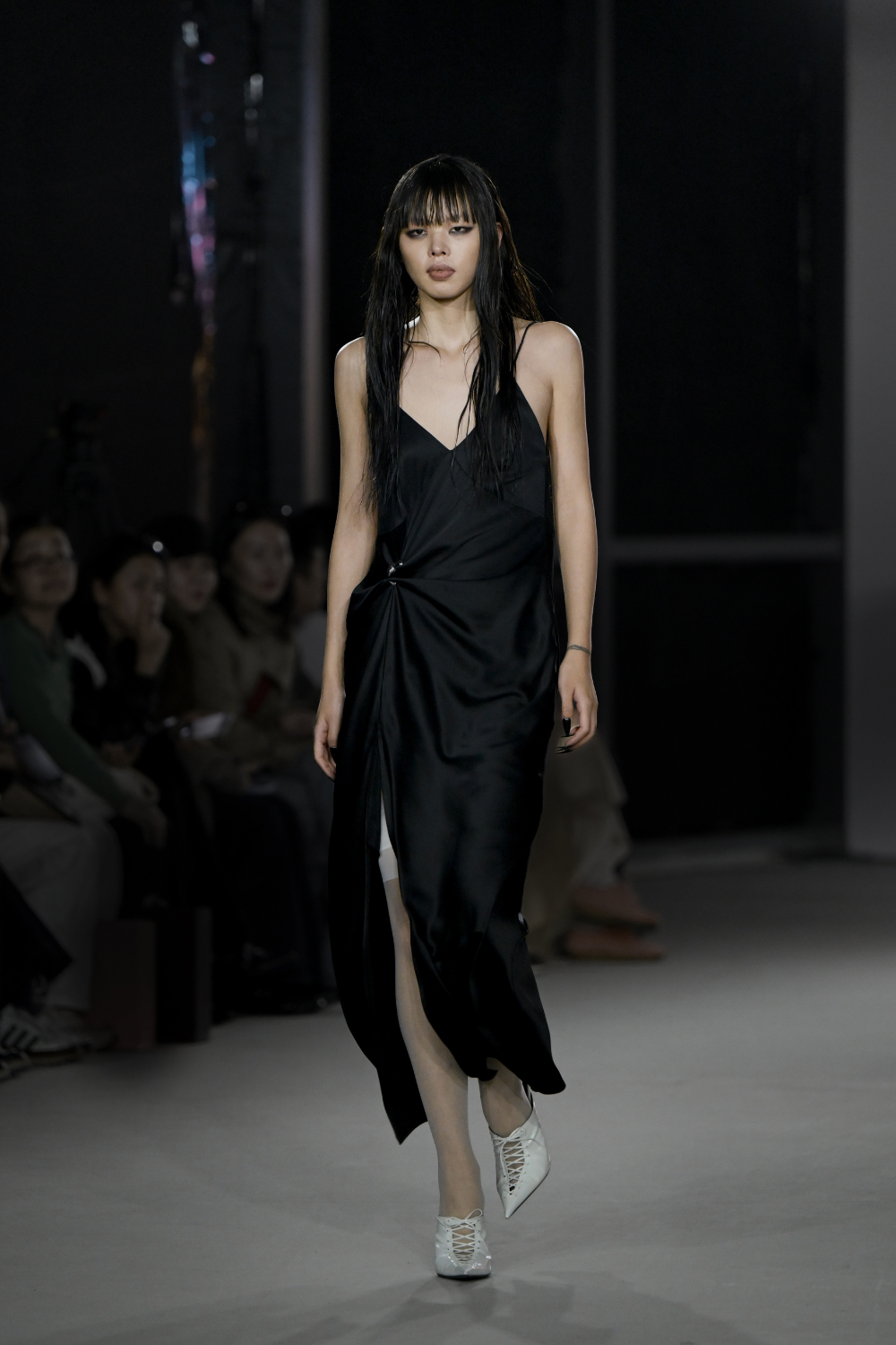 Model walking runway in the Pierced Cowlback Slip Dress crafted in sleek black satin with a draped front gathered by a silver ring, featuring a high slit and delicate straps, showcasing bespoke tailoring and luxury designer fashion by SHAO New York.