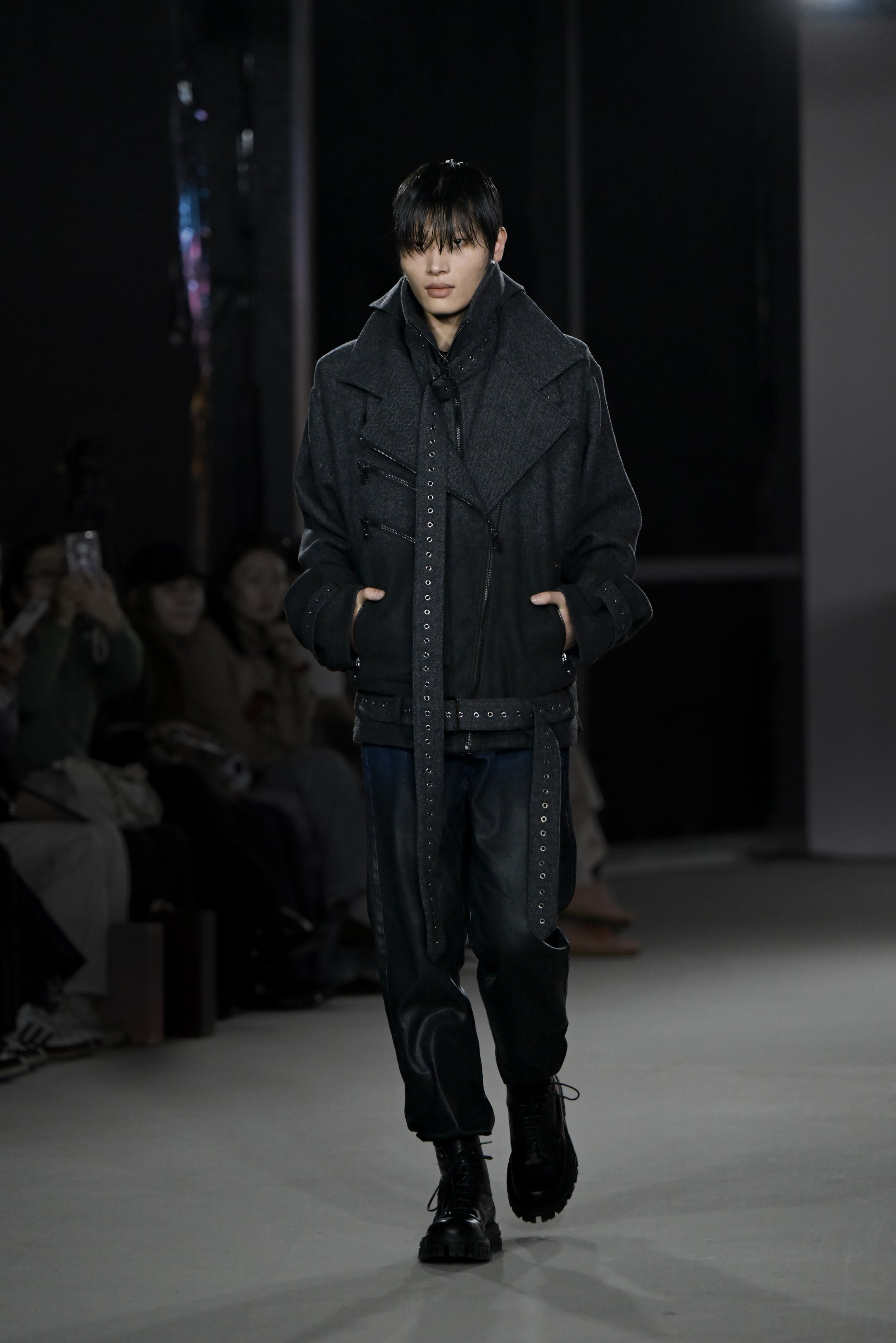 Model walking runway wearing Drop-Crotch Denim Jeans with Leather Ombre Effect styled with a layered dark jacket, featuring a sculptural silhouette and luxury designer fashion details.