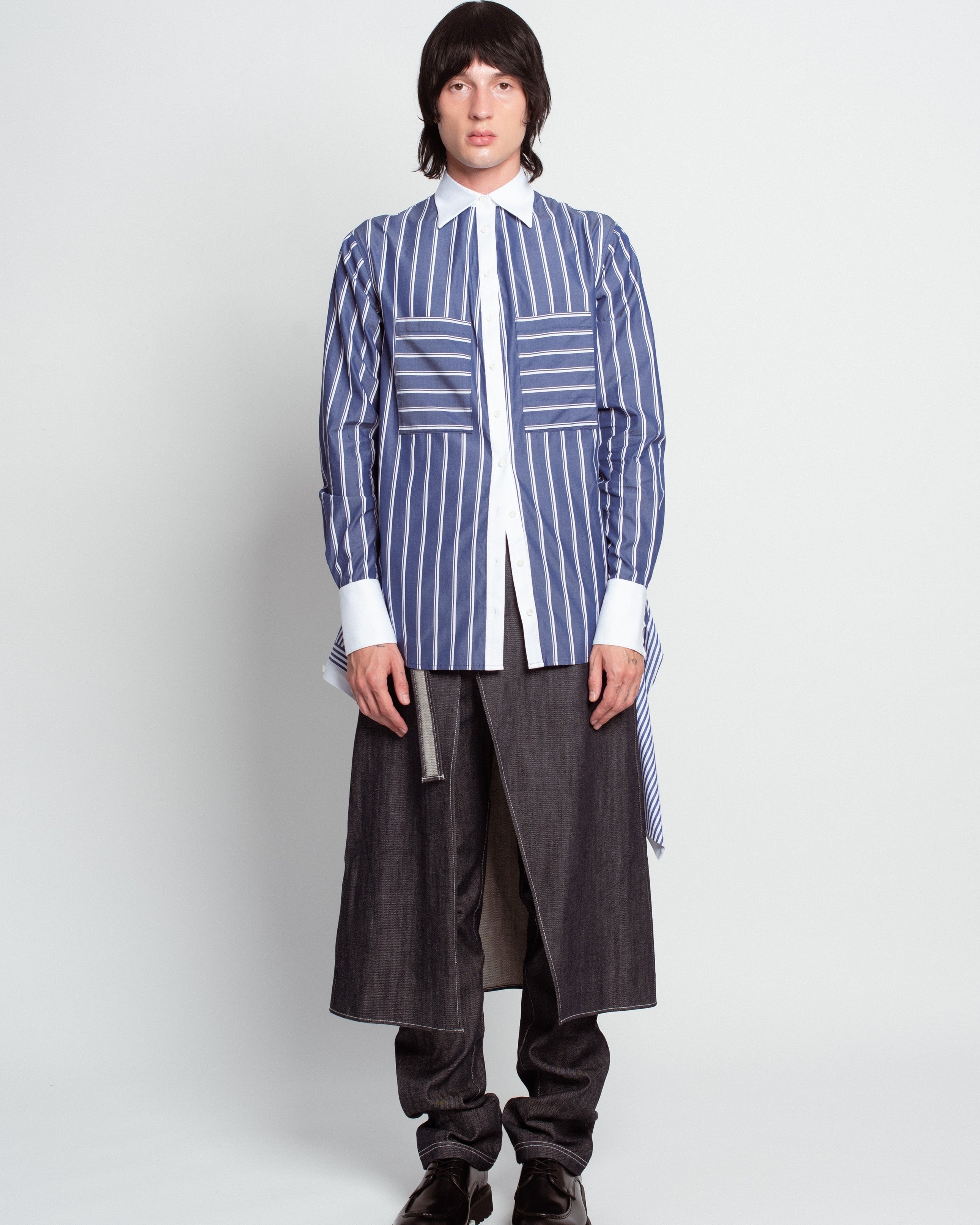 Front view of Blue Pinstripe Layered Shirt – Attached Back Construction in bold blue and white stripes, highlighted by oversized horizontal front pockets, crisp white collar and cuffs, paired with layered dark tailored trousers, embodying SHAO New York luxury designer fashion and bespoke tailoring with a sculptural silhouette.