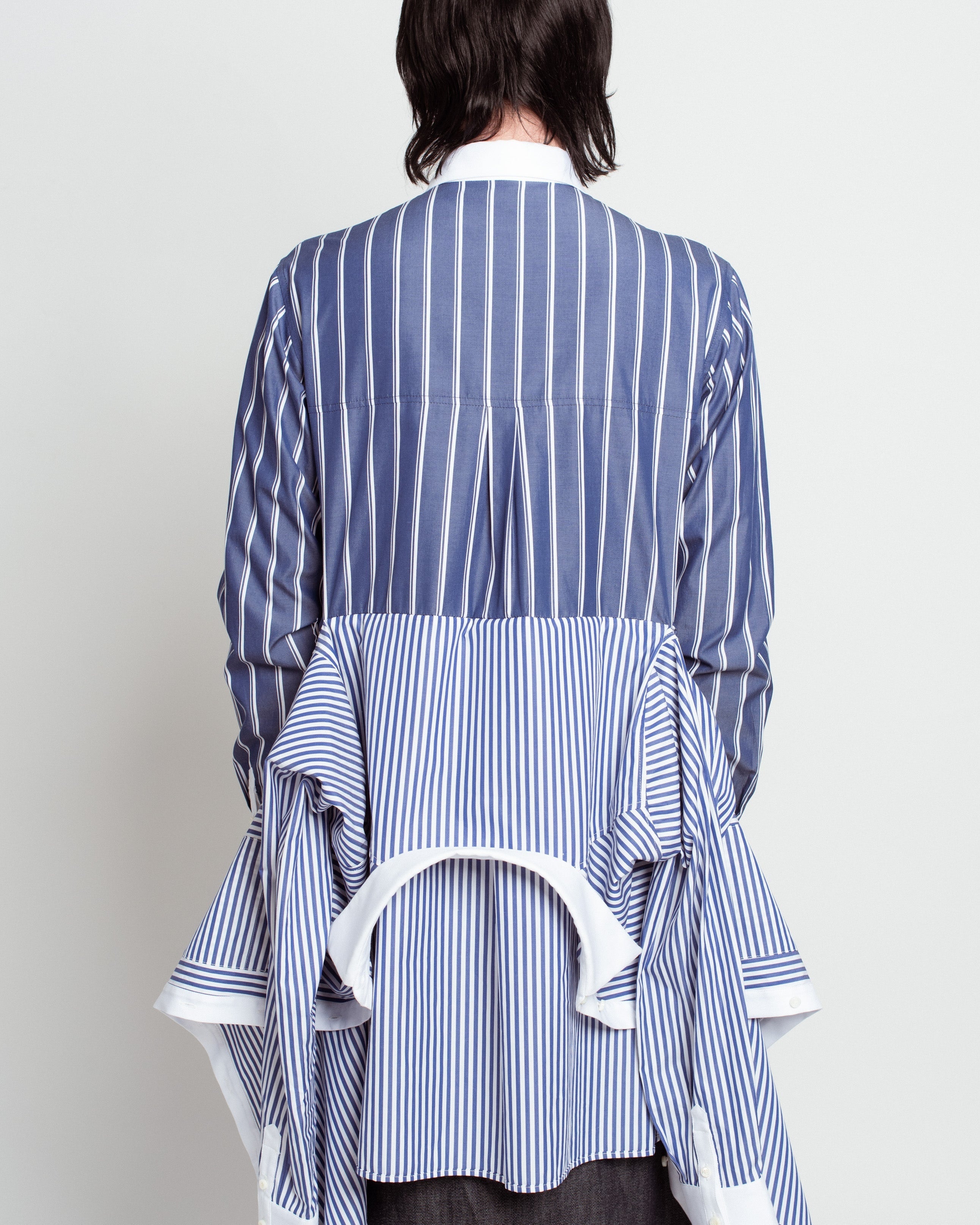 Back view of Blue Pinstripe Layered Shirt – Attached Back Construction featuring contrasting vertical stripes, draped layered fabric detail, crisp white collar and cuffs, showcasing SHAO New York bespoke tailoring and sculptural silhouette.