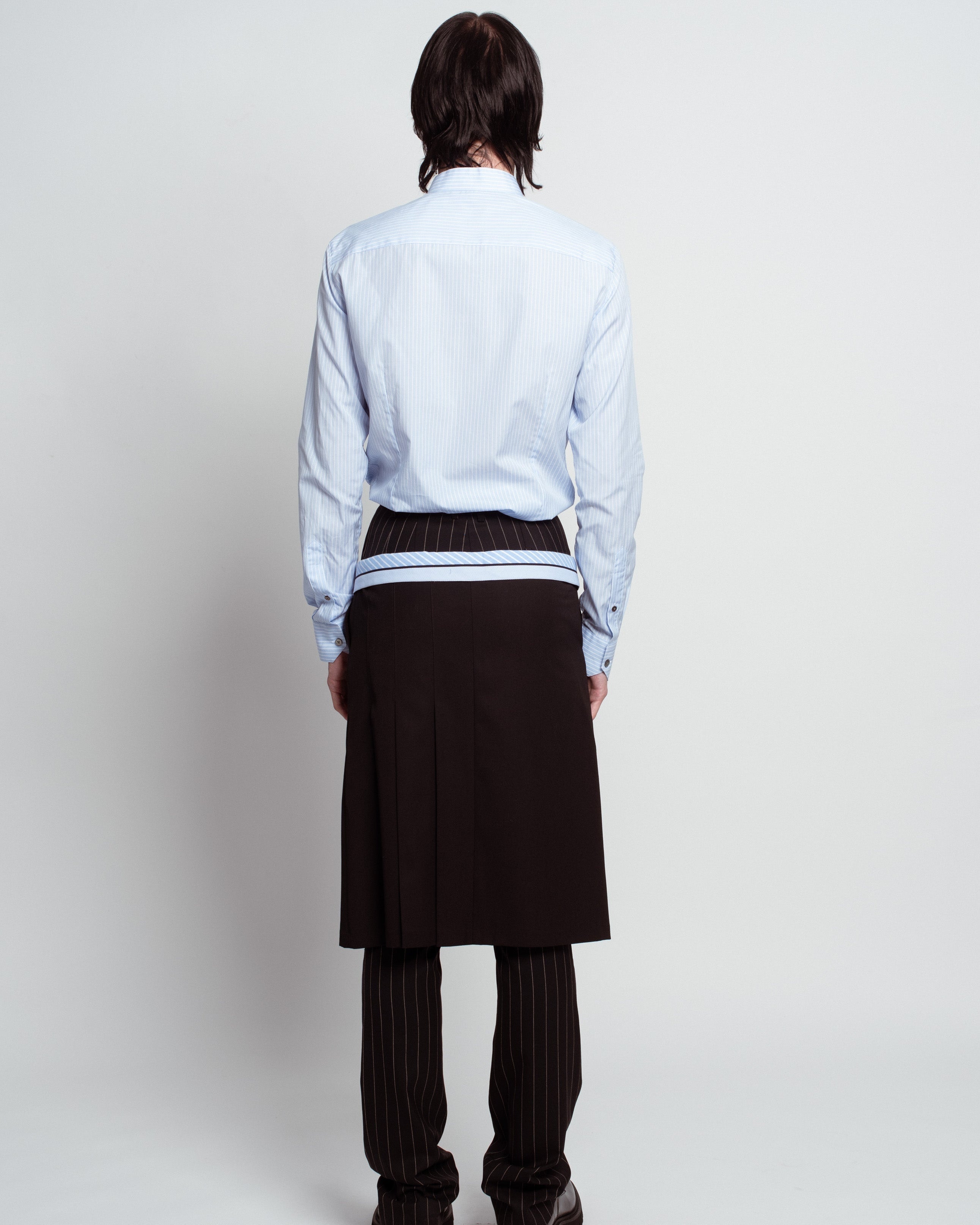 Back view of Blue Striped Band Collar Shirt in pale blue featuring fine vertical stripes and tailored fit, styled with layered pinstriped trousers and sculptural black skirt panel, reflecting SHAO New York bespoke tailoring and luxury designer fashion.