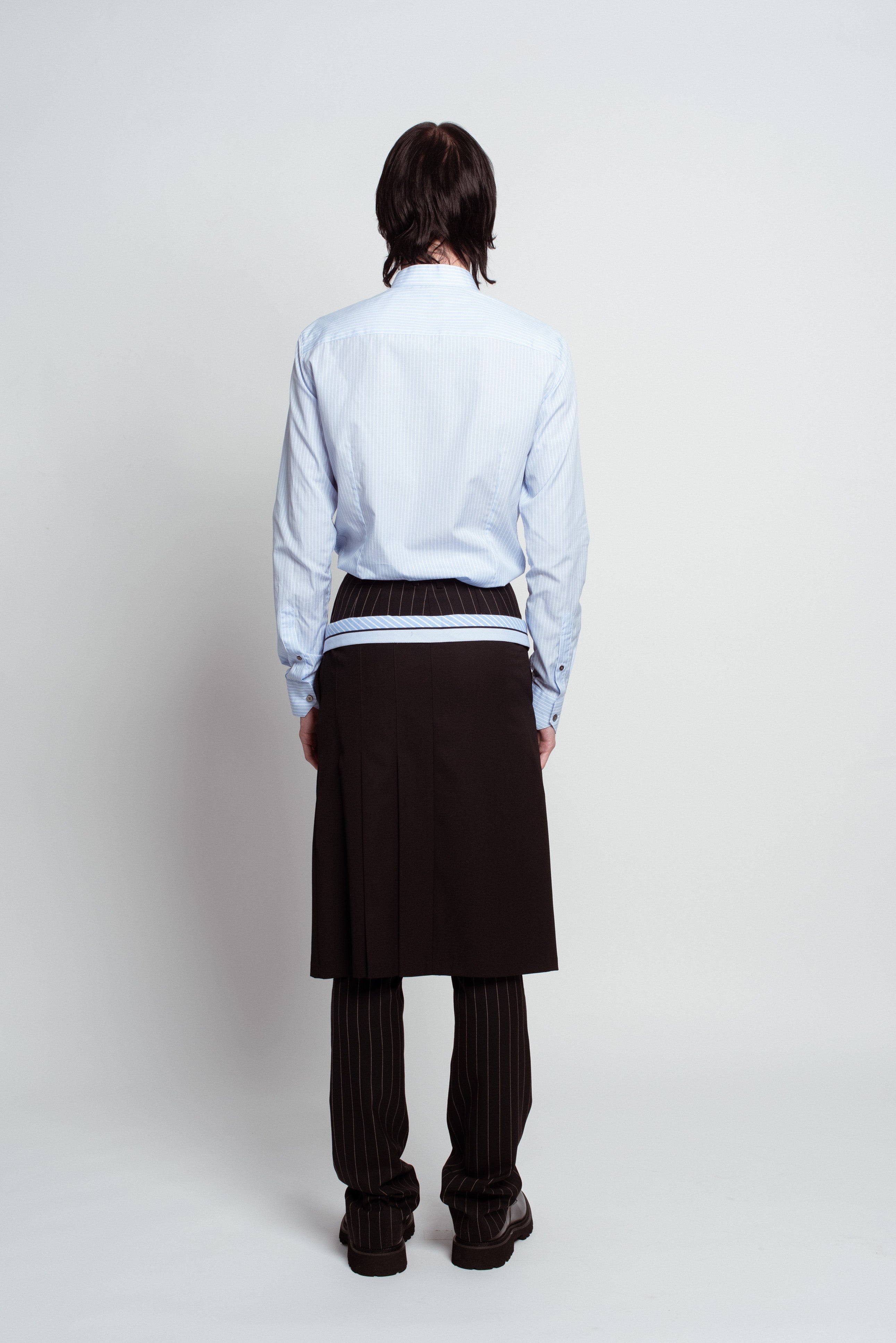 Back view of Blue Striped Band Collar Shirt in pale blue featuring fine vertical stripes and tailored fit, styled with layered pinstriped trousers and sculptural black skirt panel, reflecting SHAO New York bespoke tailoring and luxury designer fashion.