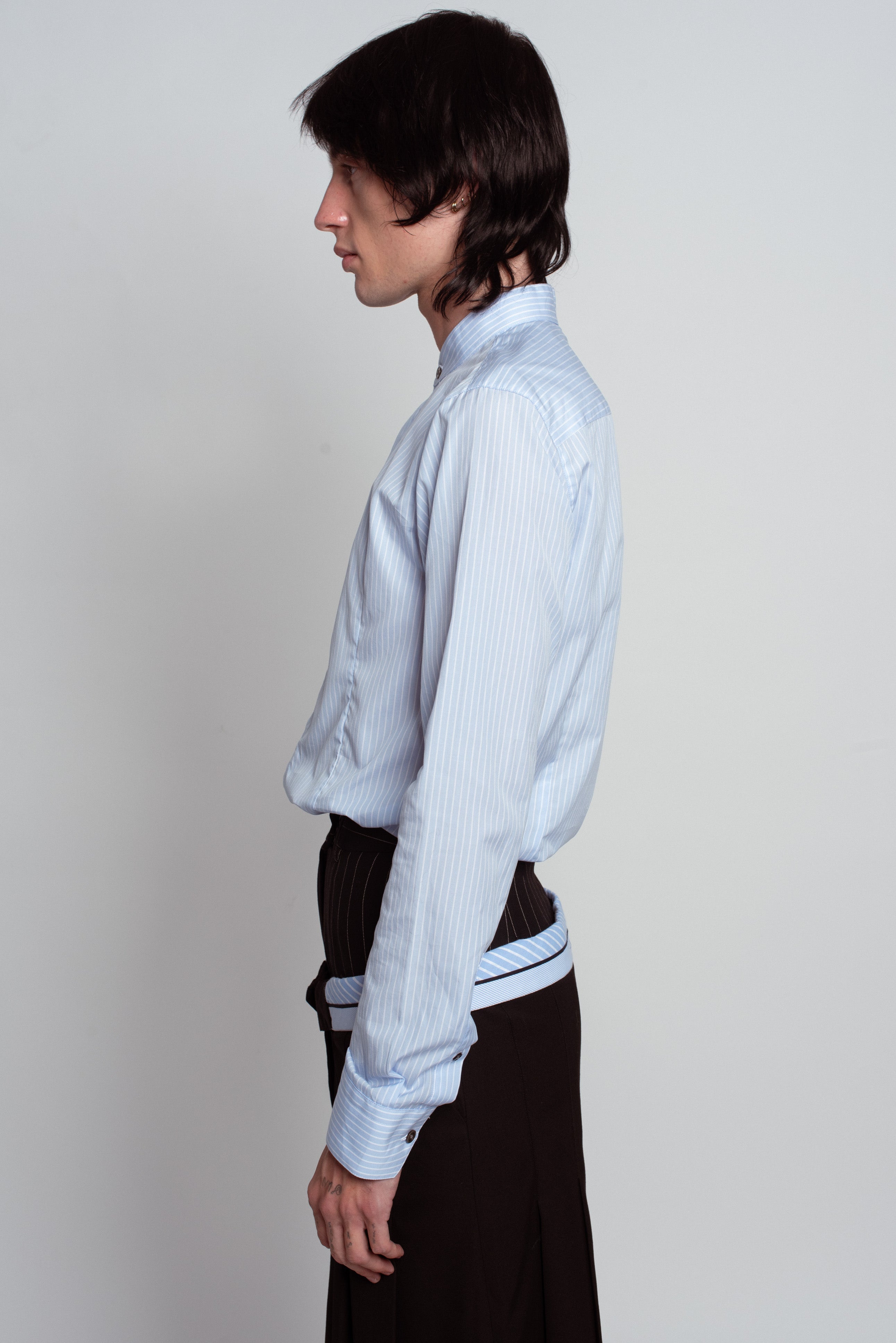 Side profile of Blue Striped Band Collar Shirt in light blue with fine vertical stripes, tailored fit, and buttoned cuffs, styled elegantly with high-waisted dark trousers, reflecting SHAO New York bespoke tailoring and luxury designer fashion.