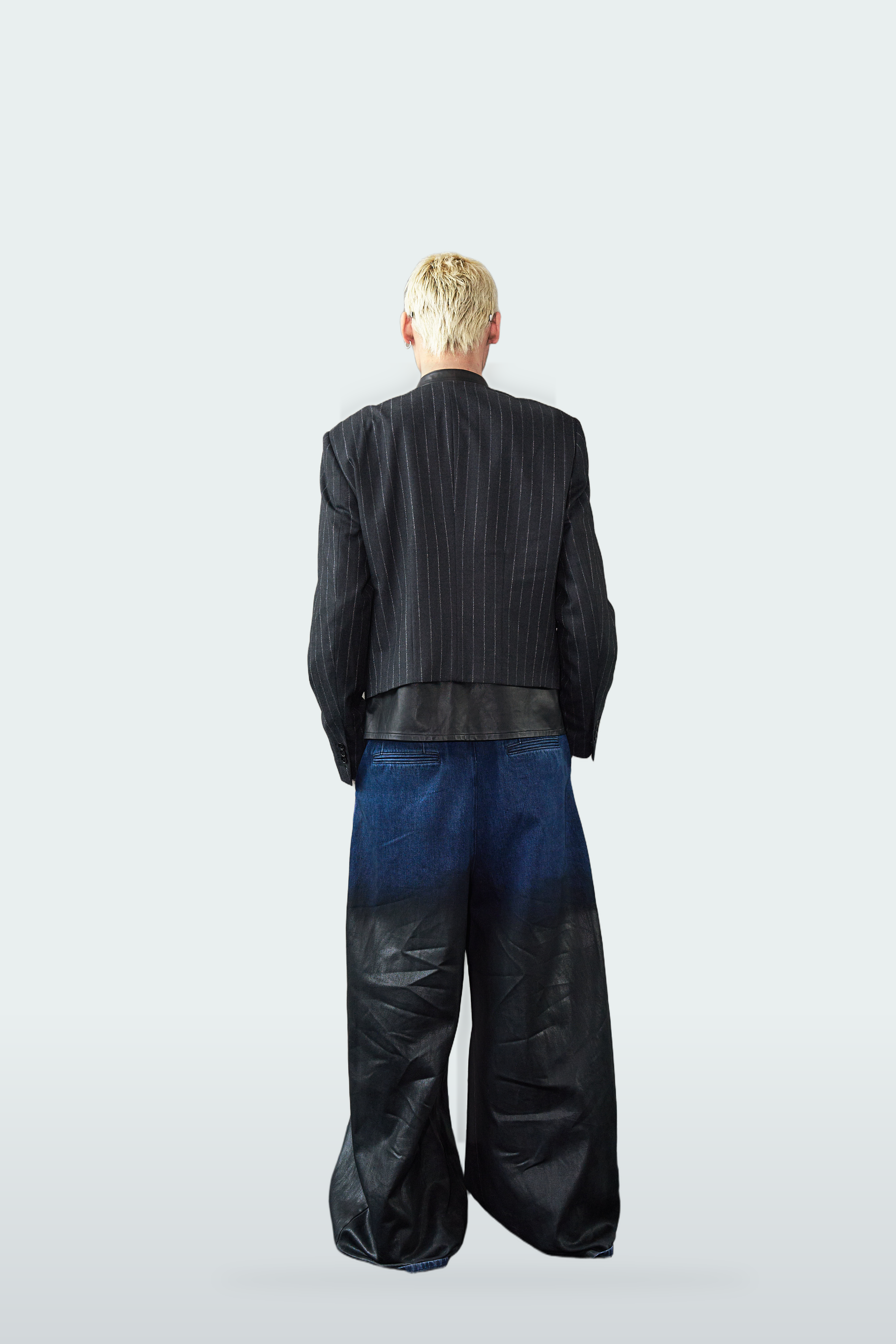 A model shown from the back wearing a black pinstripe jacket and wide-leg jeans with a dark blue to black gradient wash, set against a light gray studio background.