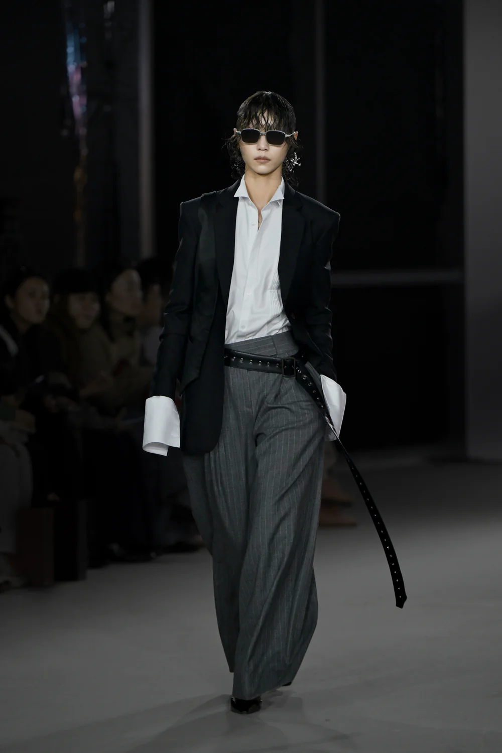 Model wearing Black Trompe L'Oeil Blazer with Satin Vest Overlay styled with a white shirt featuring extended cuffs, gray wide-leg pinstripe trousers, a long black belt, and dark sunglasses, showcasing SHAO New York bespoke tailoring and luxury designer fashion.