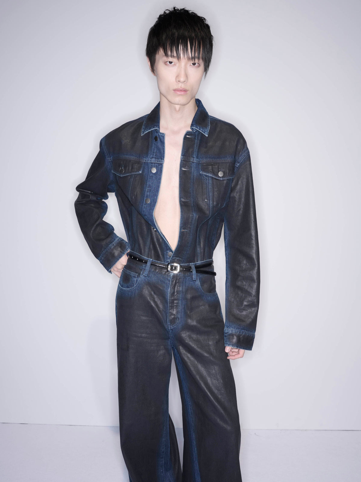 A person wearing a dark denim jumpsuit with a black belt