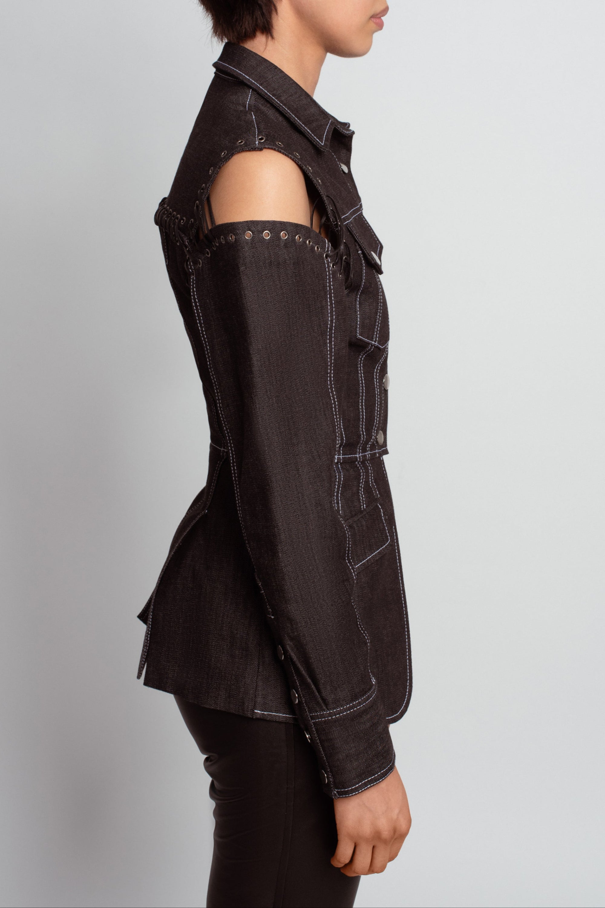 Side view of Midnight Blue Architectural Denim Jacket – Detachable Sleeve Design featuring exposed grommet detailing at the shoulders, tailored seams, and contrasting stitching for a modern sculptural silhouette.
