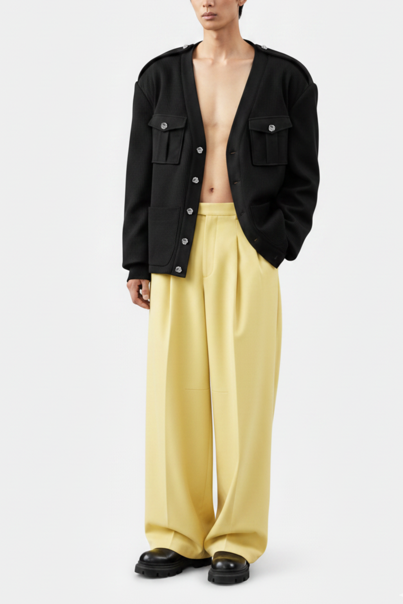 Front view of Black Military-Style Utility Cardigan featuring prominent flap pockets, silver buttons, and structured epaulets paired with loose pale yellow trousers, showcasing SHAO New York bespoke tailoring and luxury designer fashion.