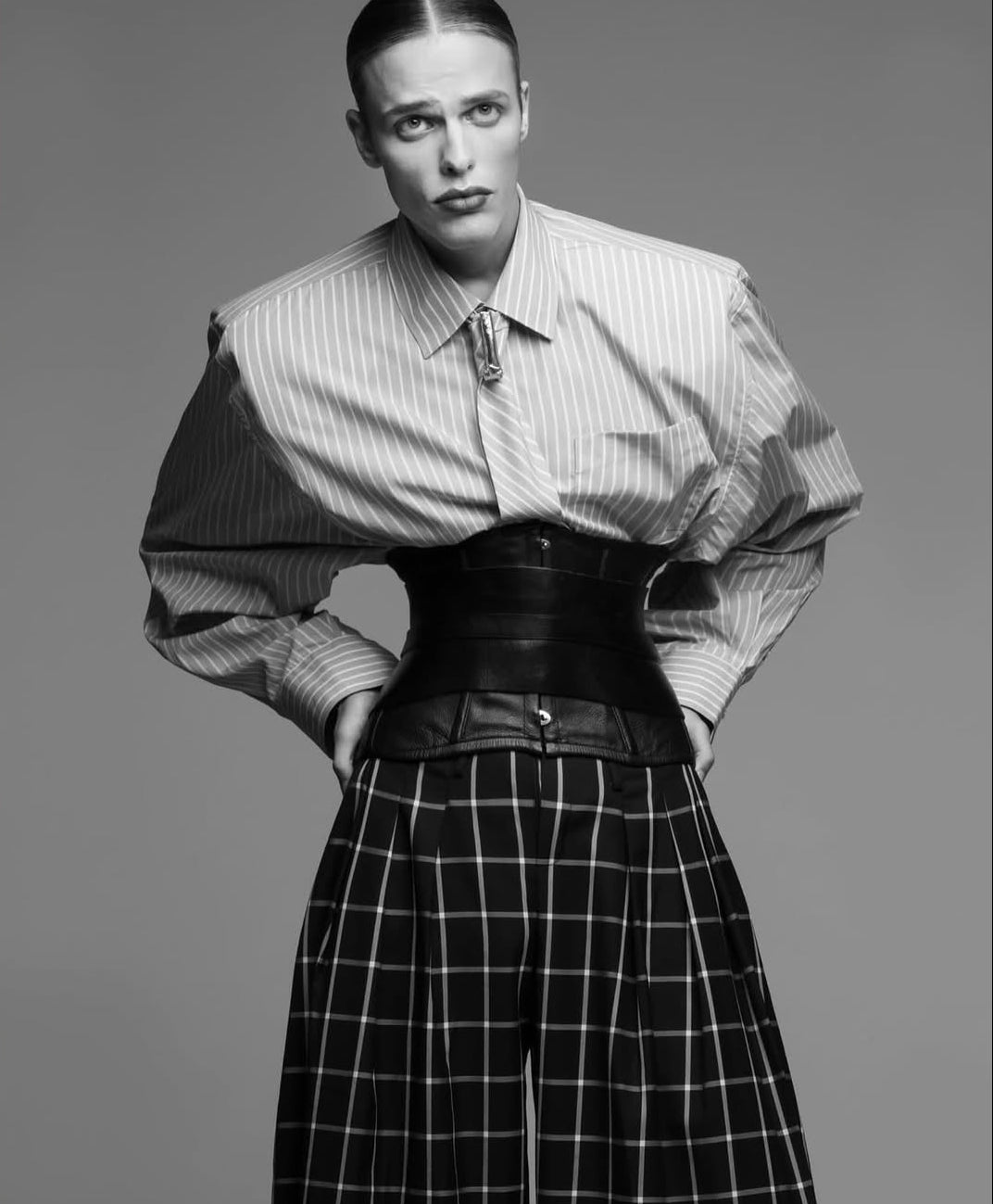 Person wearing a striped shirt and checkered pants with a belt, on a gray background