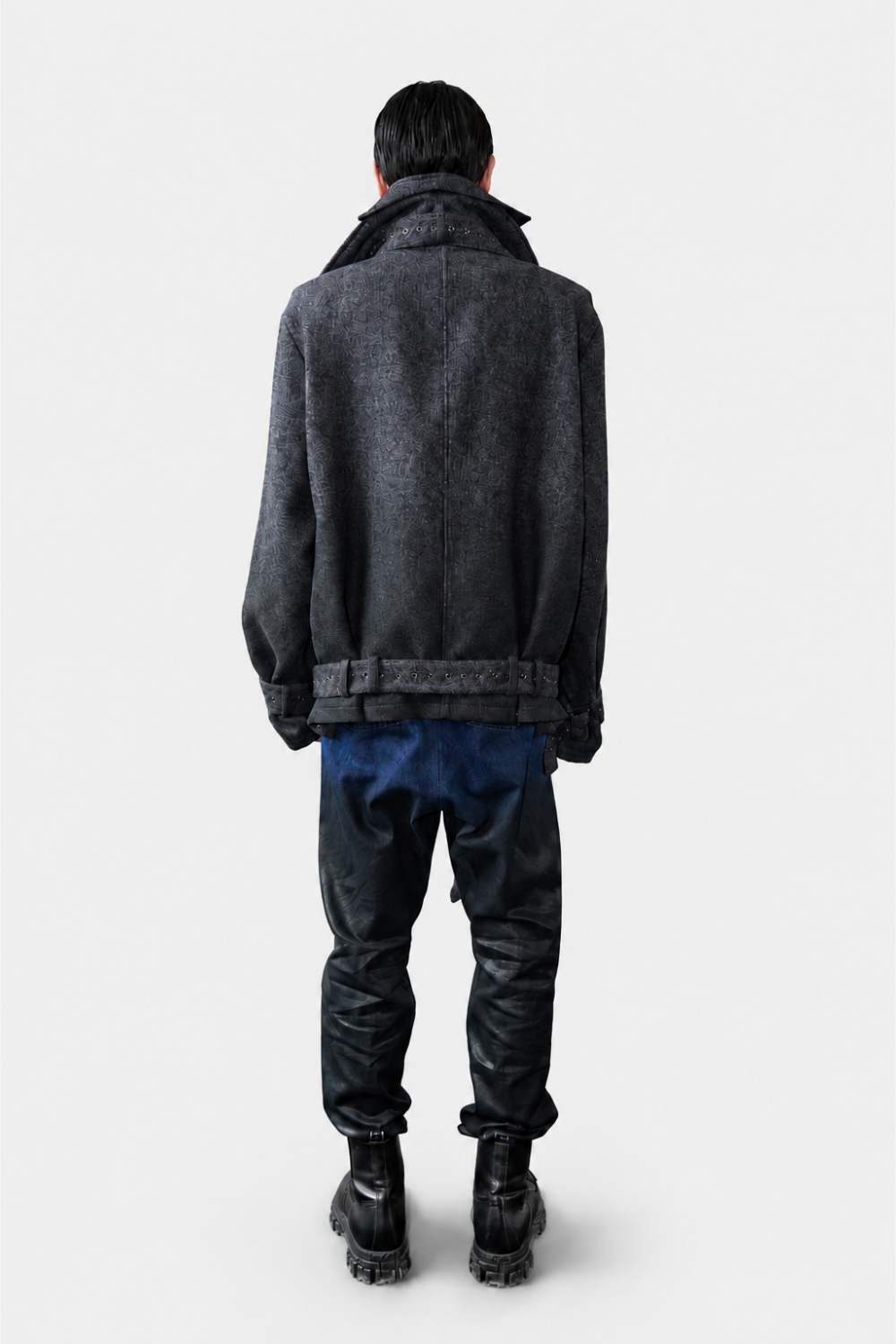 Model seen from the back wearing Drop-Crotch Denim Jeans with Leather Ombre Effect in a deep blue to black gradient, paired with a textured dark oversized jacket and chunky black boots, showcasing a sculptural silhouette in luxury designer fashion.