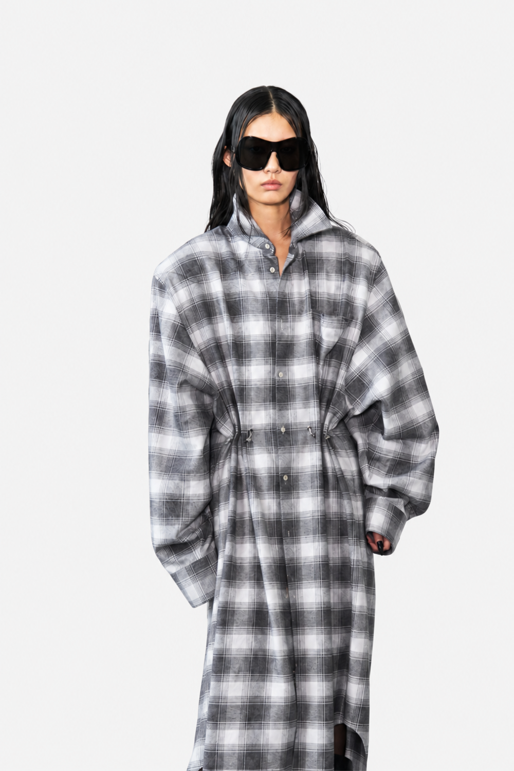 Model wearing the Oversized Flannel Shirt Dress in black and white plaid, featuring voluminous sleeves, a high collar, and an adjustable cinched waist for a contemporary sculptural silhouette.