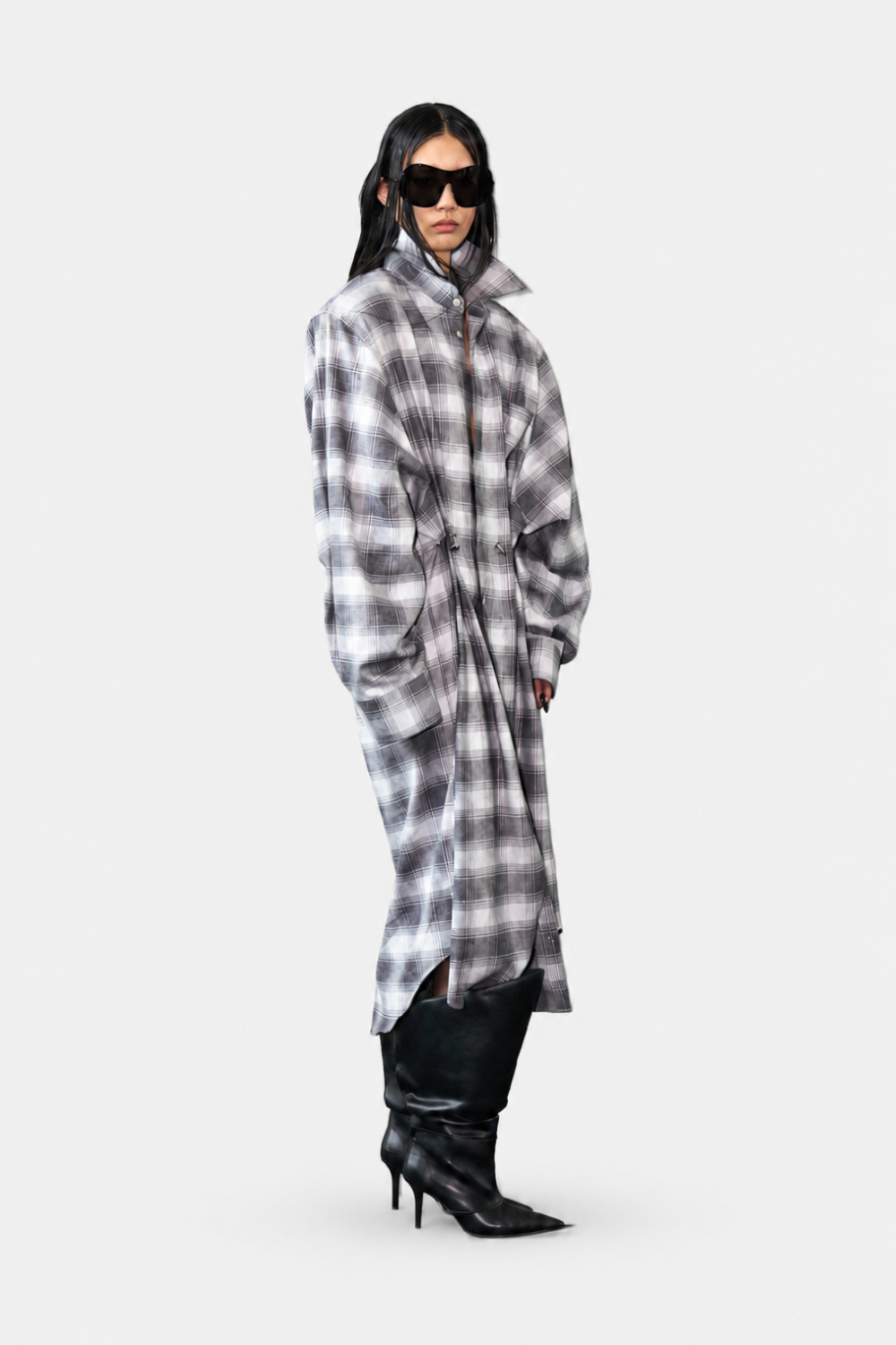 Model wearing the Oversized Flannel Shirt Dress in muted gray tones, styled with a high collar, relaxed silhouette, cinched waist, and paired with black heeled boots and dark sunglasses for a modern sculptural look.