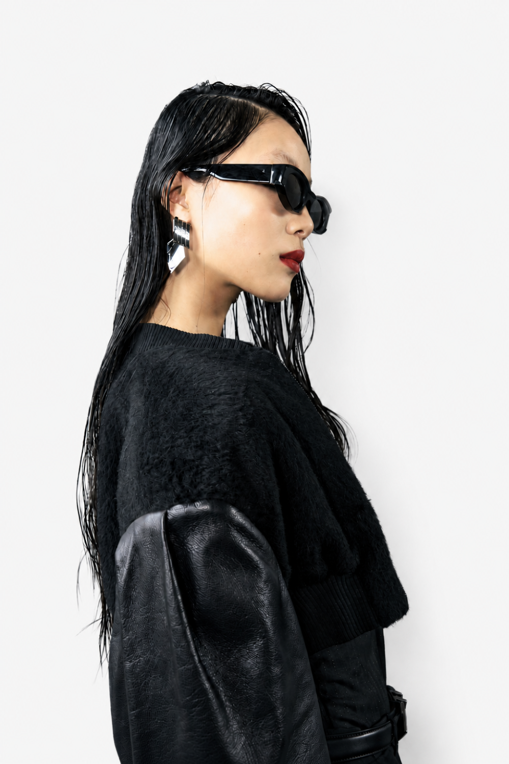 Side profile of a model wearing the Cropped Alpaca and Leather Bomber Jacket with wet-look hair, bold geometric earrings, and dark sunglasses, highlighting SHAO New York’s sculptural silhouette and luxury bespoke tailoring.