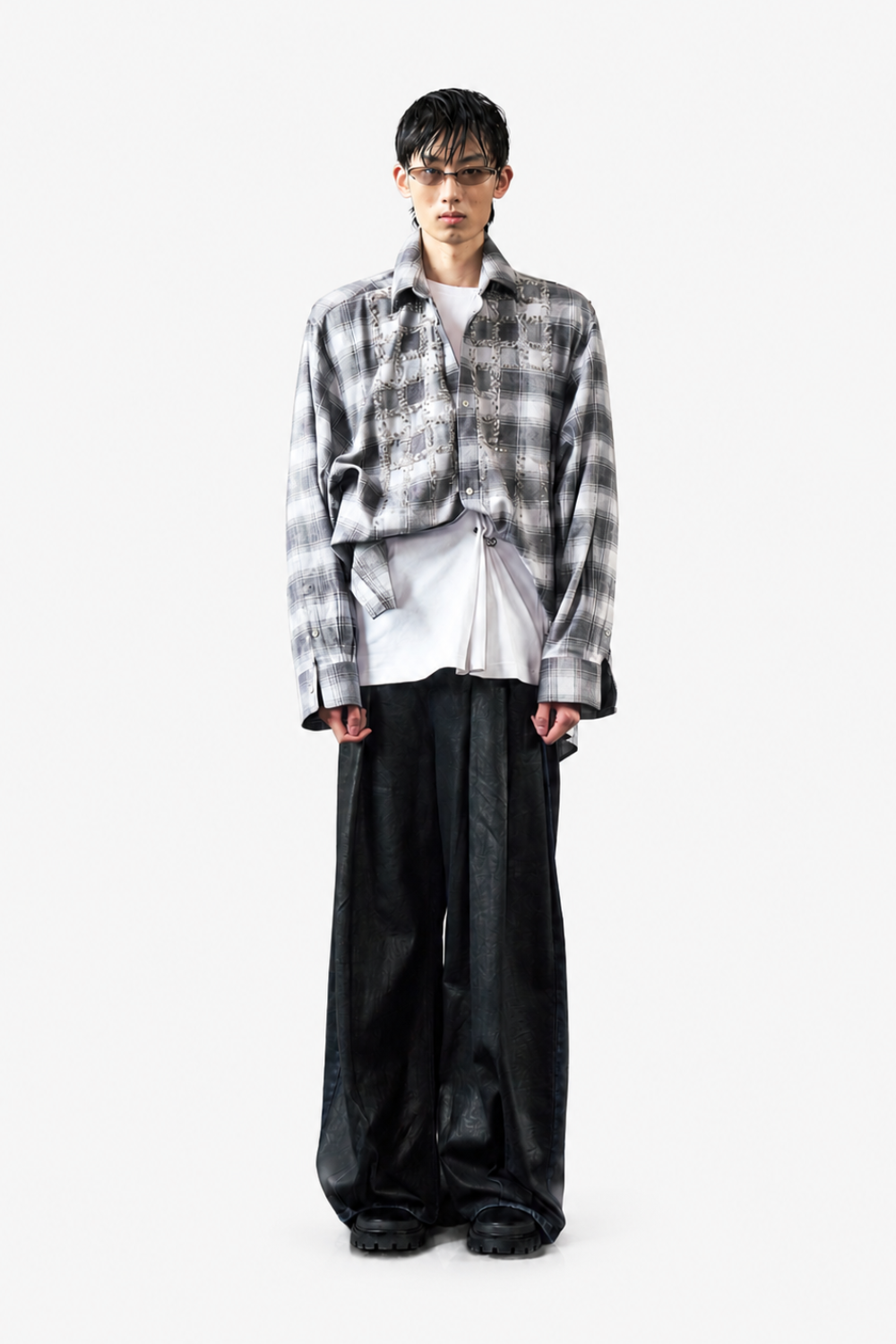 Model wearing the Pierced Vintage T-Shirt - White layered under a distressed grey plaid shirt with oversized cuffs, paired with wide-leg black trousers and dark chunky shoes for a modern, edgy look.