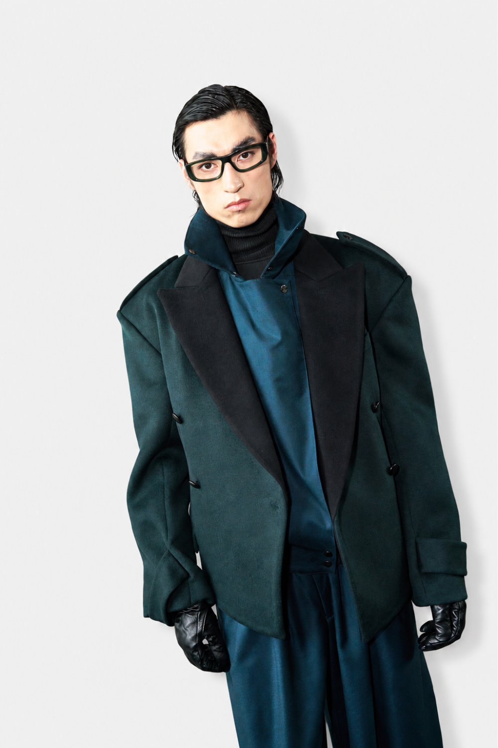Model wearing Wool Barrel Pleated Trousers - Emerald paired with an oversized dark teal tailored jacket featuring bold lapels and structured shoulders, embodying SHAO New York luxury designer fashion and sculptural silhouette.