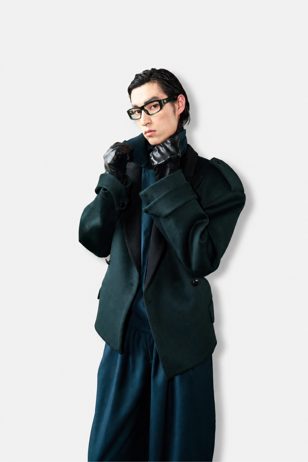 Model wearing Wool Barrel Pleated Trousers - Emerald styled with a dark tailored jacket featuring structured shoulders, paired with black leather gloves and bold eyewear, showcasing SHAO New York bespoke tailoring and a refined sculptural silhouette.