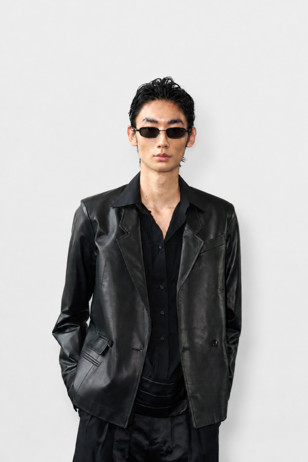 Model wearing Black Tailored Tuxedo Shirt paired with a sleek black leather blazer and slim black trousers, styled with dark sunglasses for a modern sculptural silhouette and luxury designer fashion.