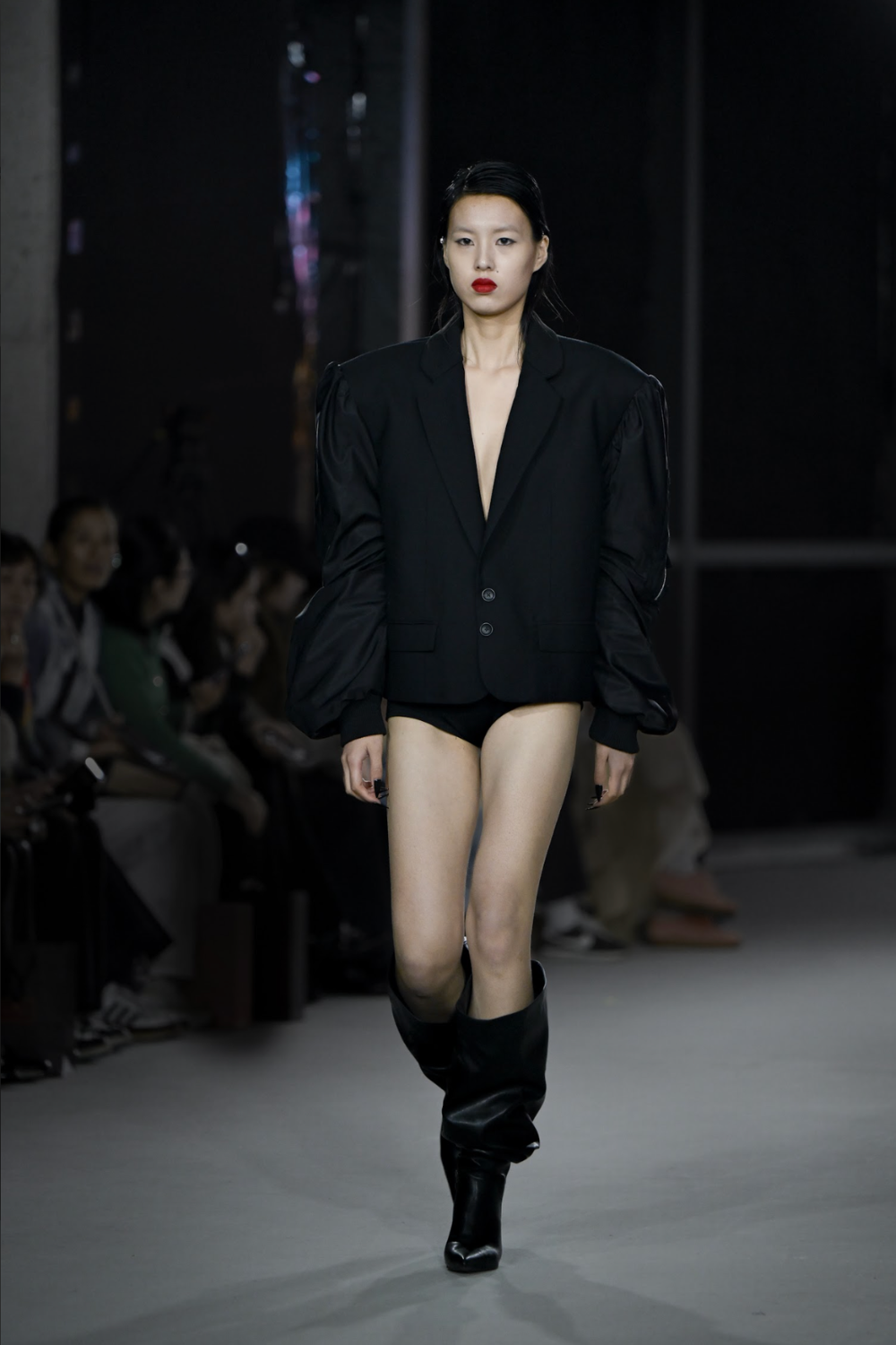 Model walking runway in the Hybrid Bomber Sleeve Blazer, featuring dramatic voluminous sleeves, sharp lapels, and a sleek sculptural silhouette, highlighting bespoke New York tailoring.