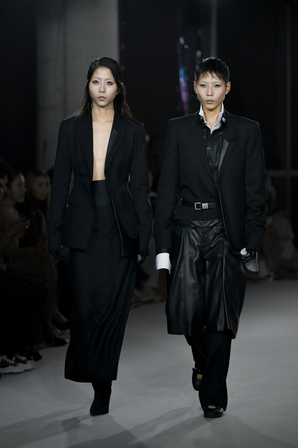 Two models walking the runway wearing the Double Layer Pinstripe Blazer, styled with sleek black tailored garments that feature modern sculptural silhouettes and luxury bespoke New York designer tailoring.