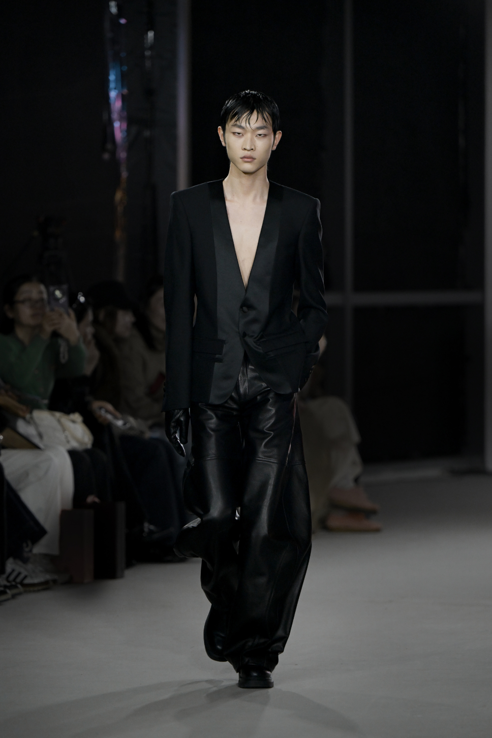 Model walking on a runway wearing a black outfit.