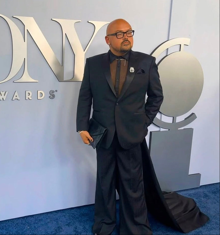 Man in a suit standing in front of a Tony Awards sign.