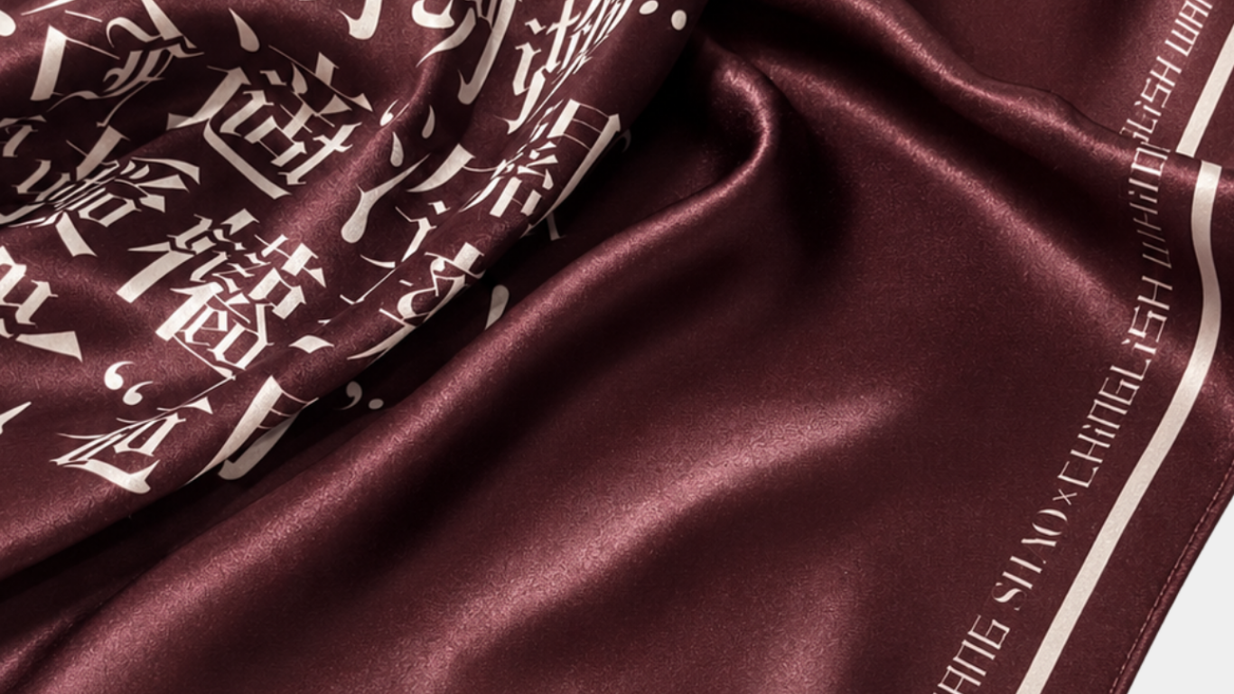 Close-up of smooth, deep burgundy fabric with white stylized Chinese characters printed on one side, featuring a subtle sheen and folded texture highlighting its silky material.