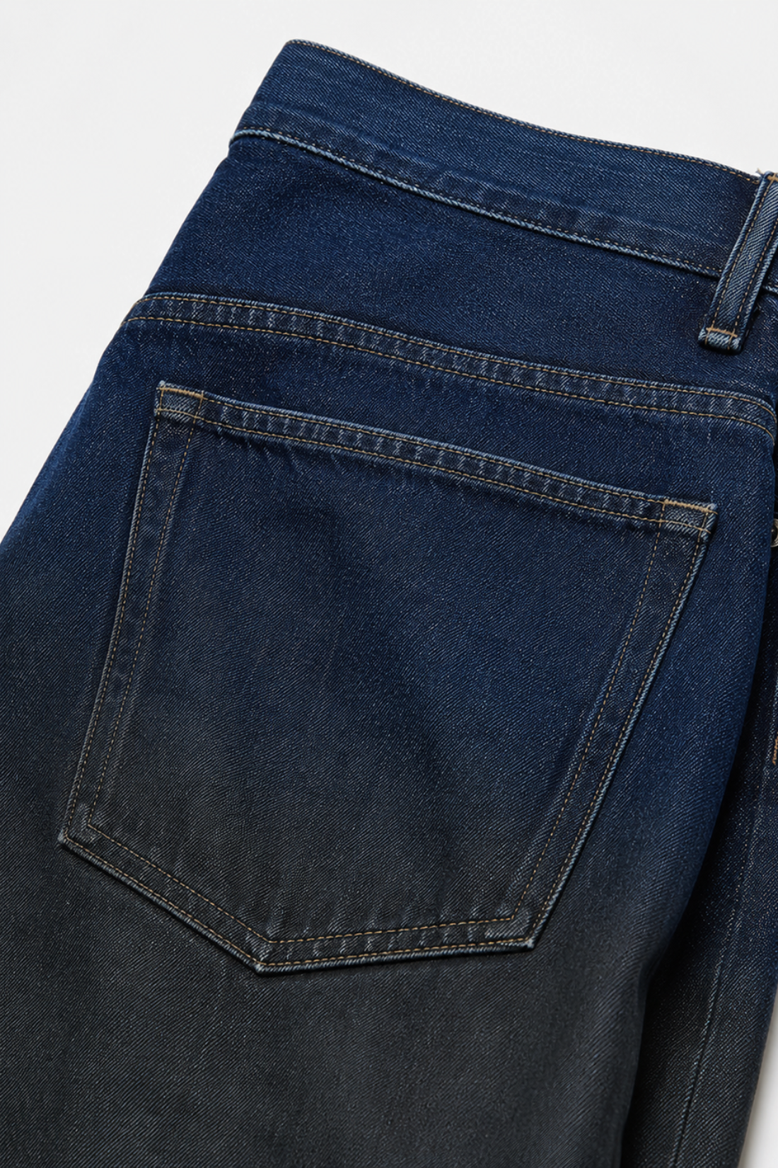 Close-up of Drop-Crotch Denim Jeans with Leather Ombre Effect showcasing deep indigo fading into black, featuring a sculptural silhouette with tailored bespoke finishing details.